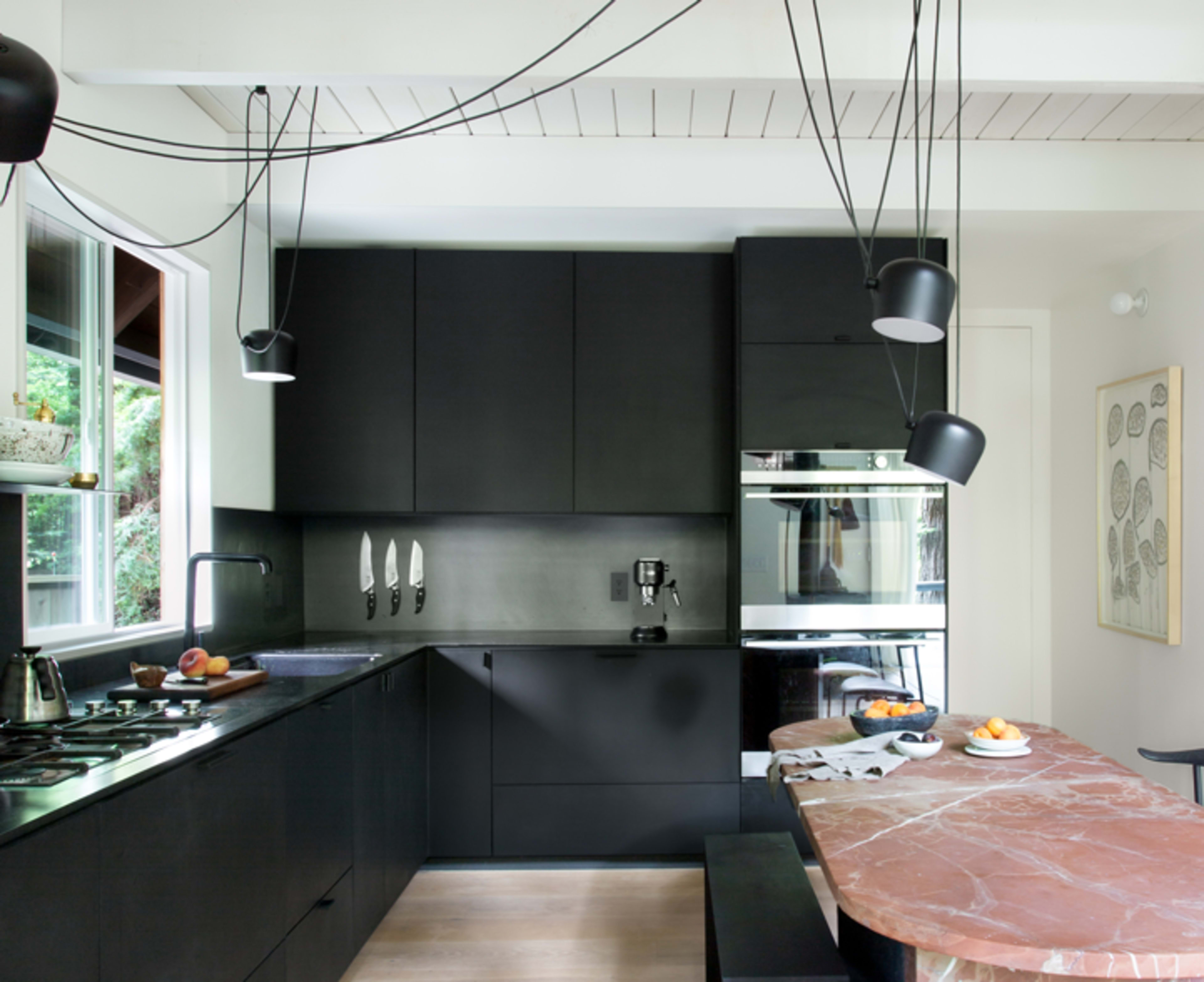 The kitchen features black cabinetry, a marble dining table, and hanging pendant lights with exposed wiring.