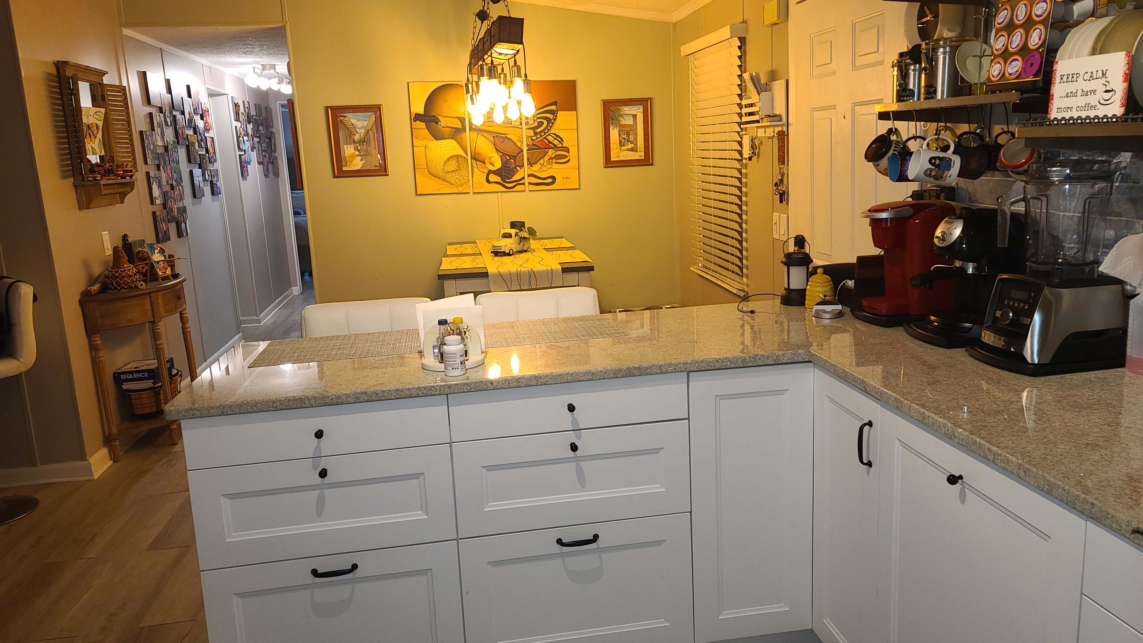A spacious kitchen features a granite countertop with white cabinetry, a coffee maker, and a dining area visible in the background.