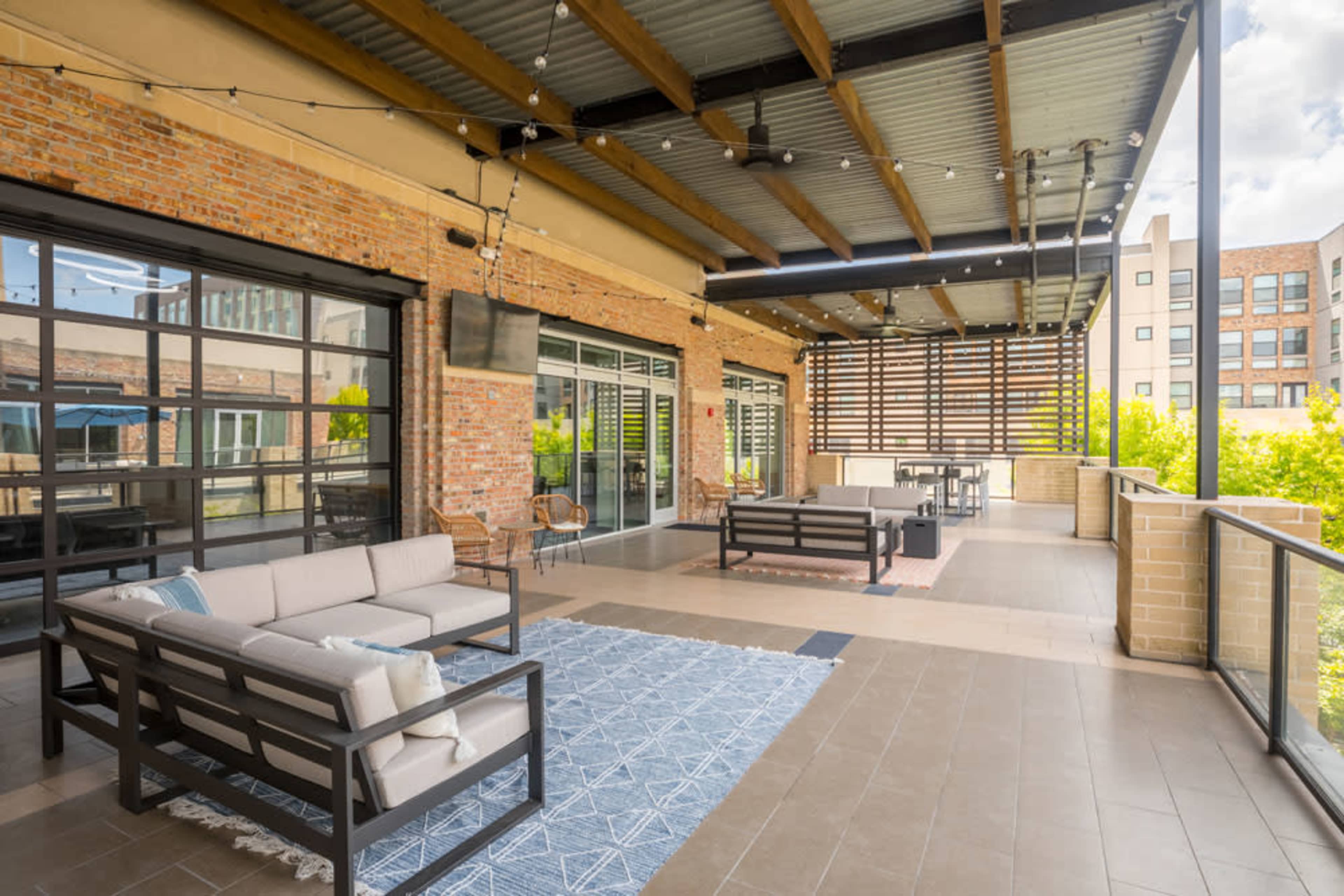 A spacious outdoor patio with modern furniture, including a couch and a rug, surrounded by brick walls and large windows.