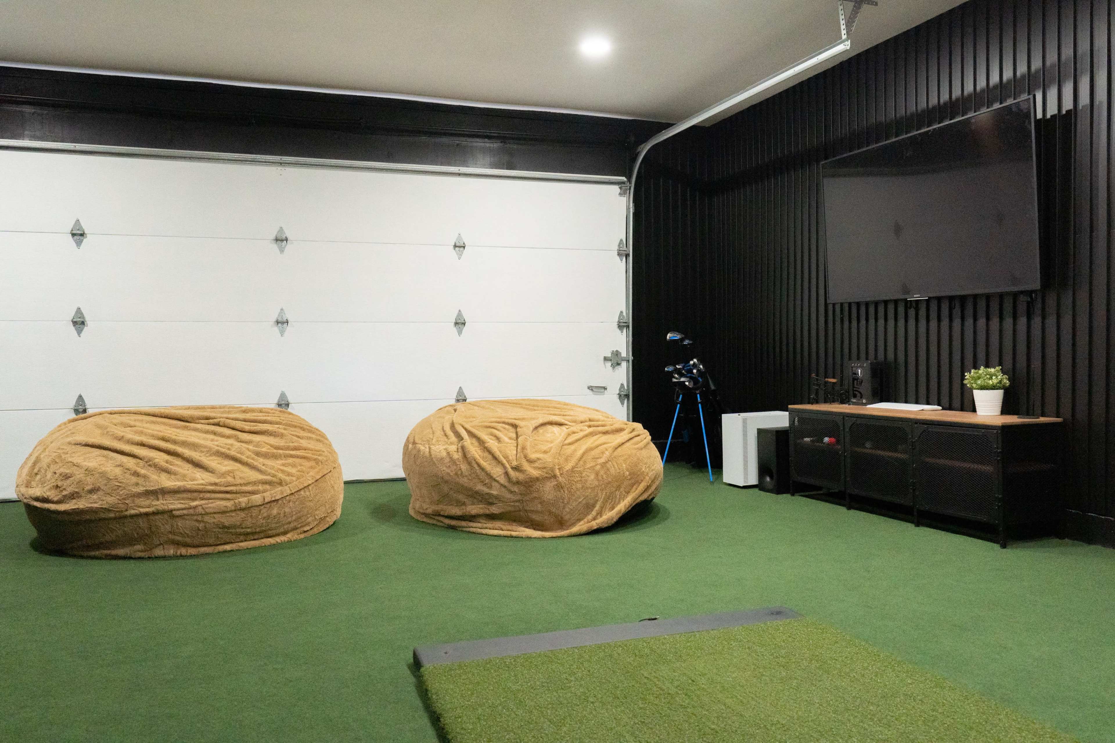 A garage interior with two large, tan bean bag chairs, a mounted television, and a small potted plant on a black media console.