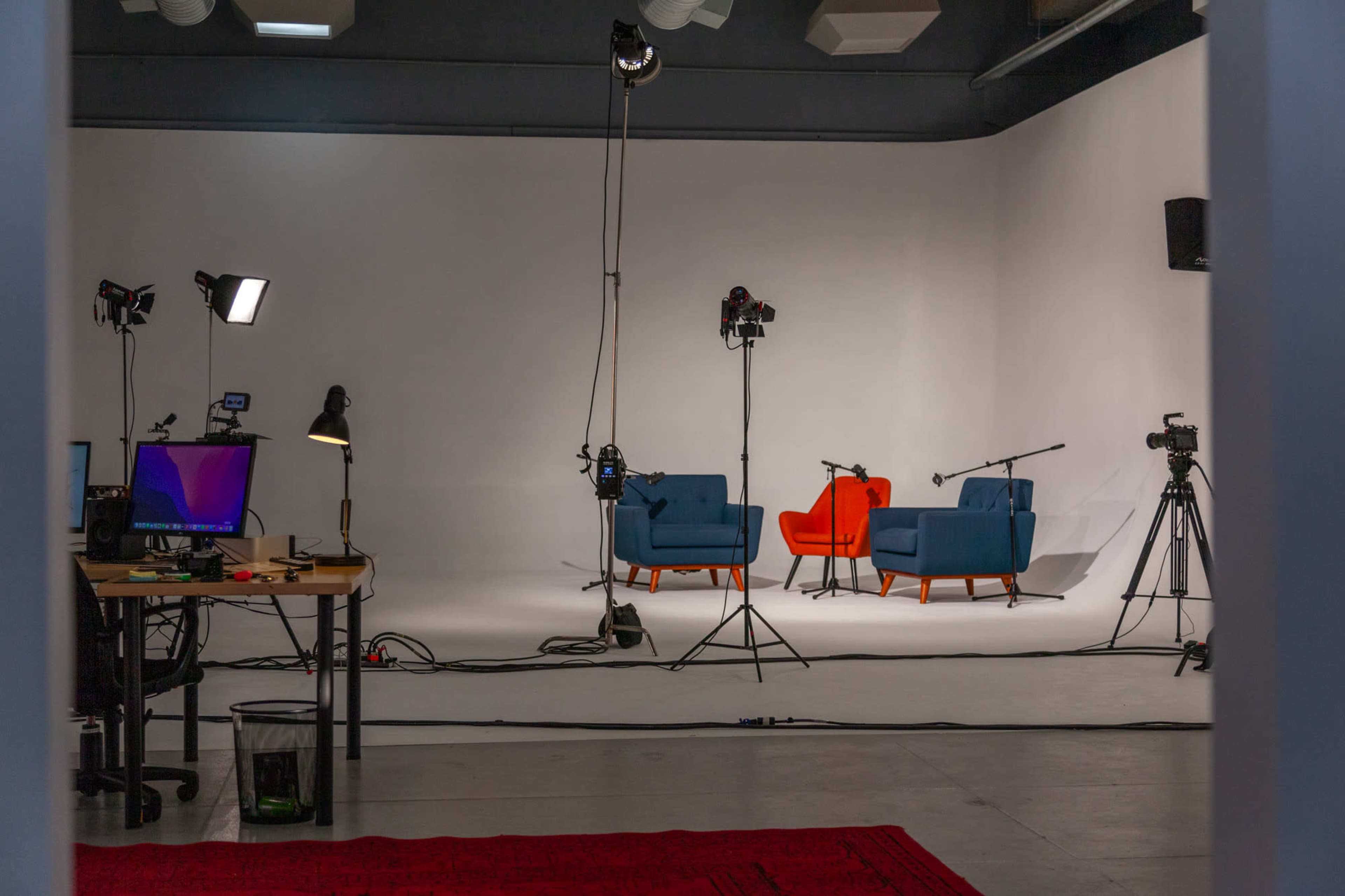 A film setup features two colorful chairs and multiple cameras positioned on tripods against a plain white backdrop.