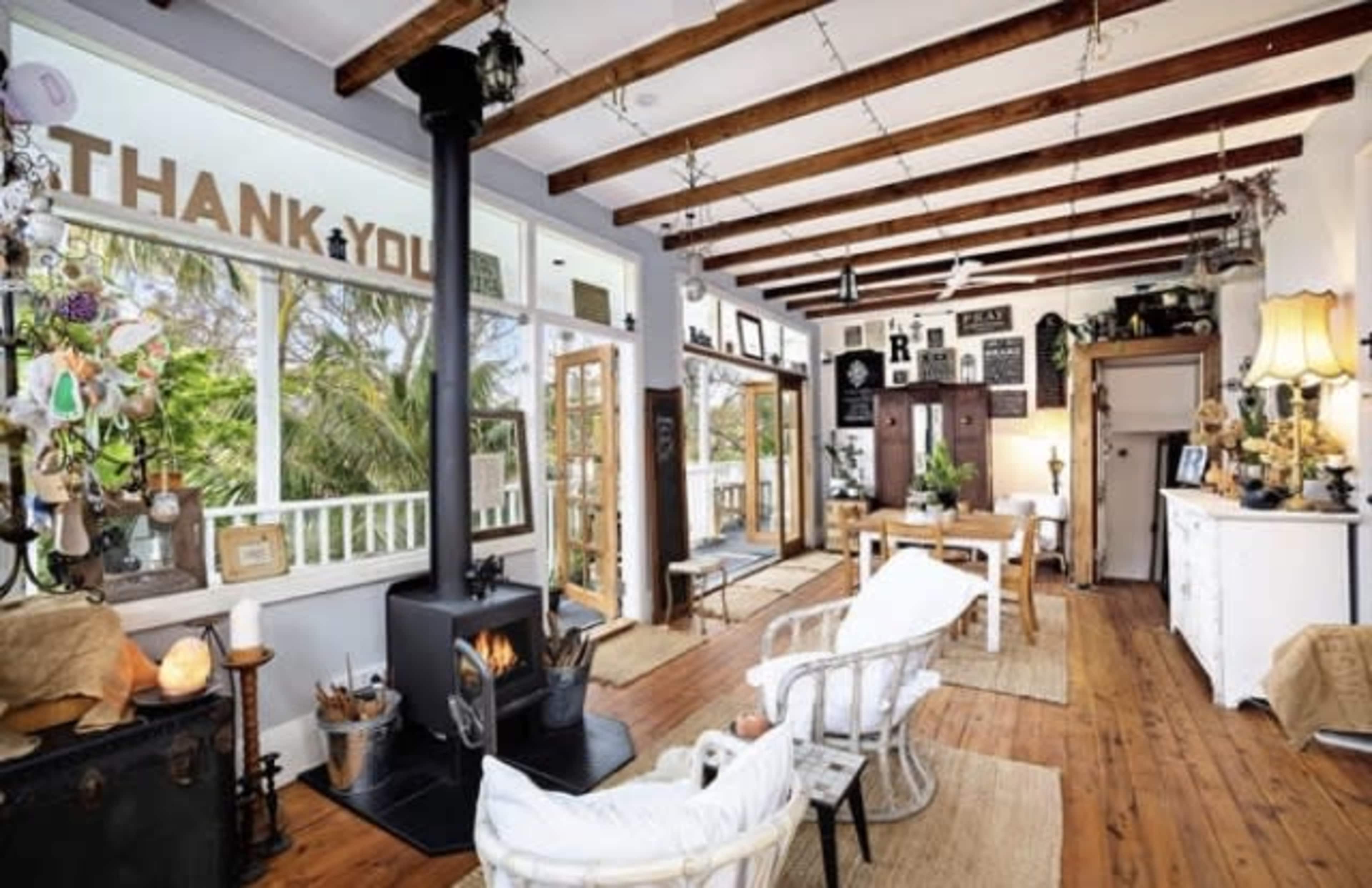 A spacious living area with wooden beams, a black stove, and a dining table surrounded by various decorative items and plants.