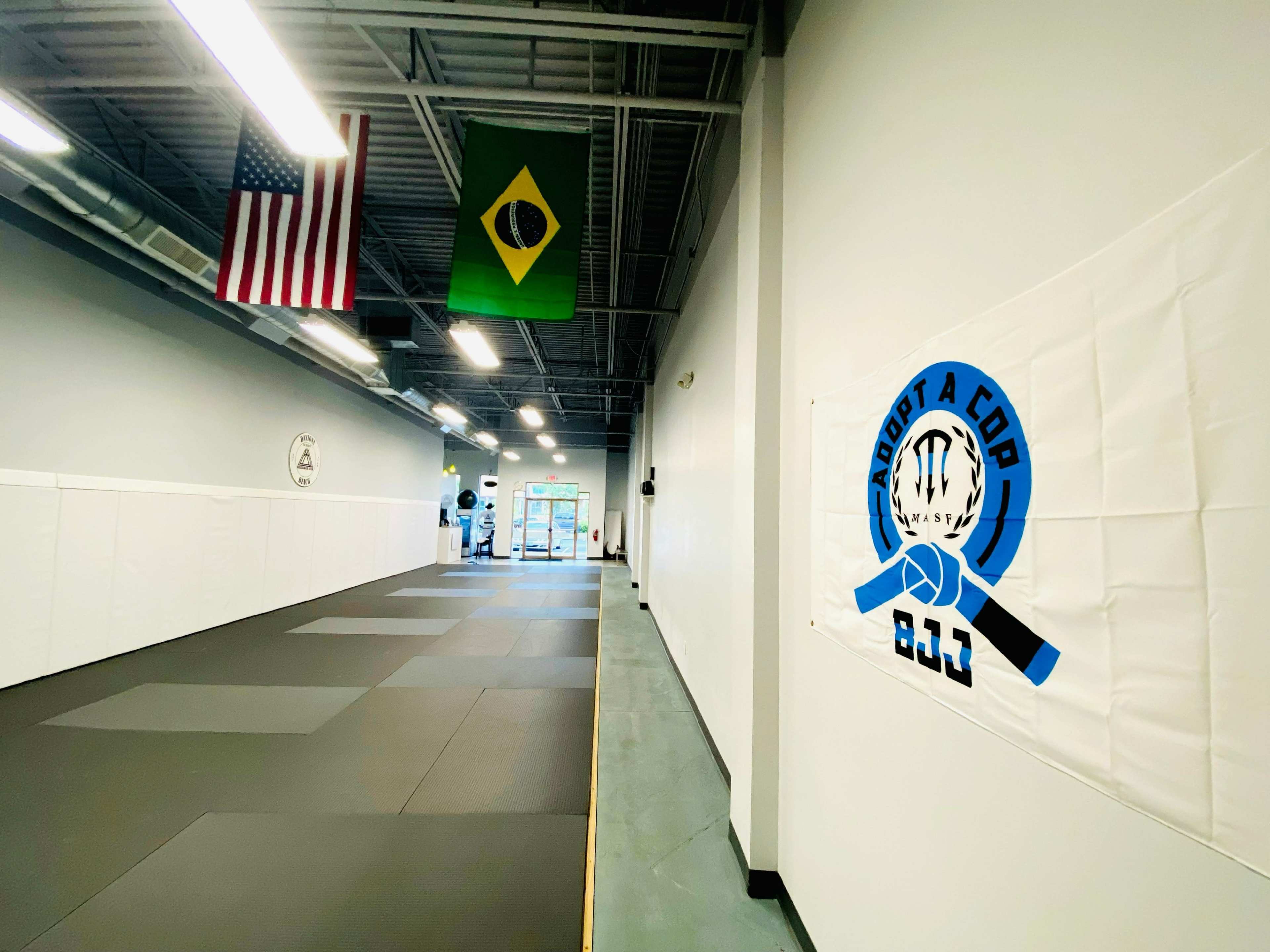 A spacious martial arts studio with American and Brazilian flags hanging from the ceiling and a large banner on the wall advertising a program.
