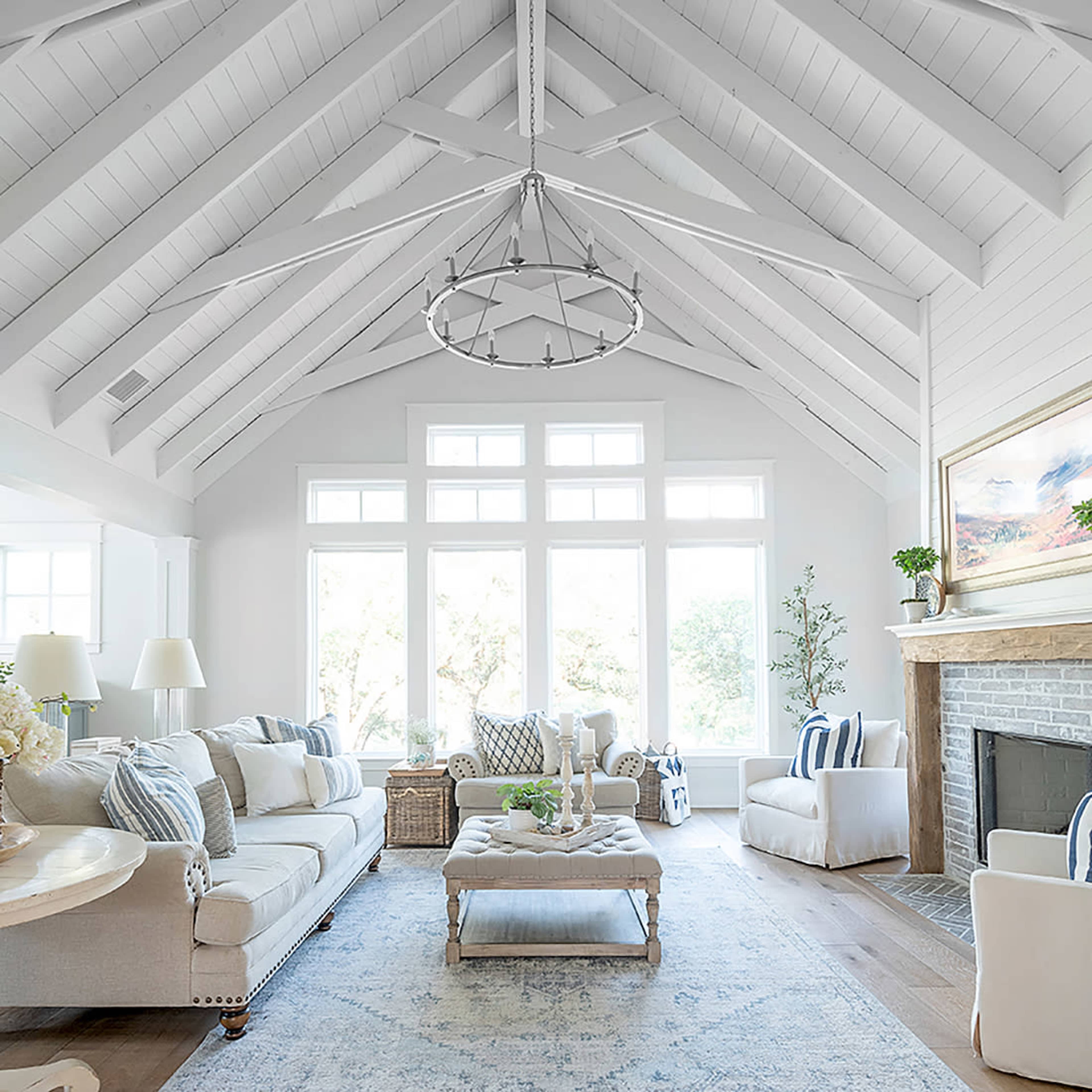 A spacious living room features a light-colored sofa, a large coffee table, and a stone fireplace beneath a vaulted ceiling with a chandelier.