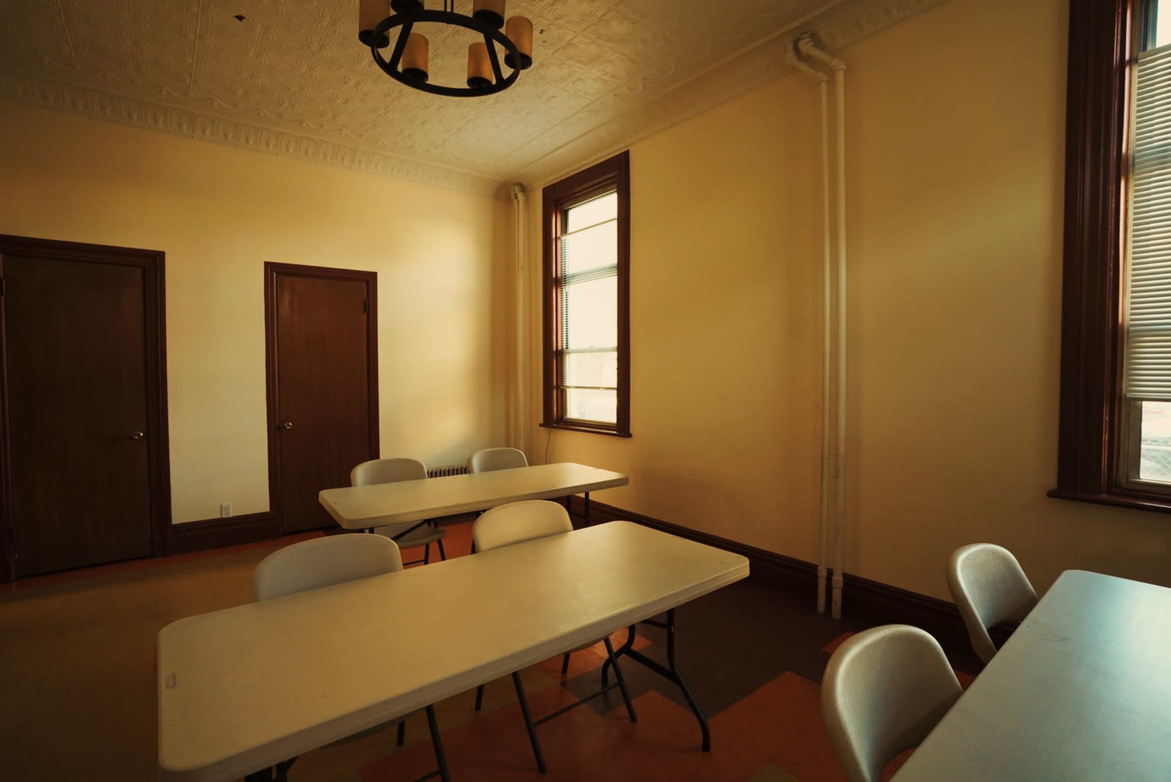 A room with two doors, several folding tables, and windows allowing natural light.