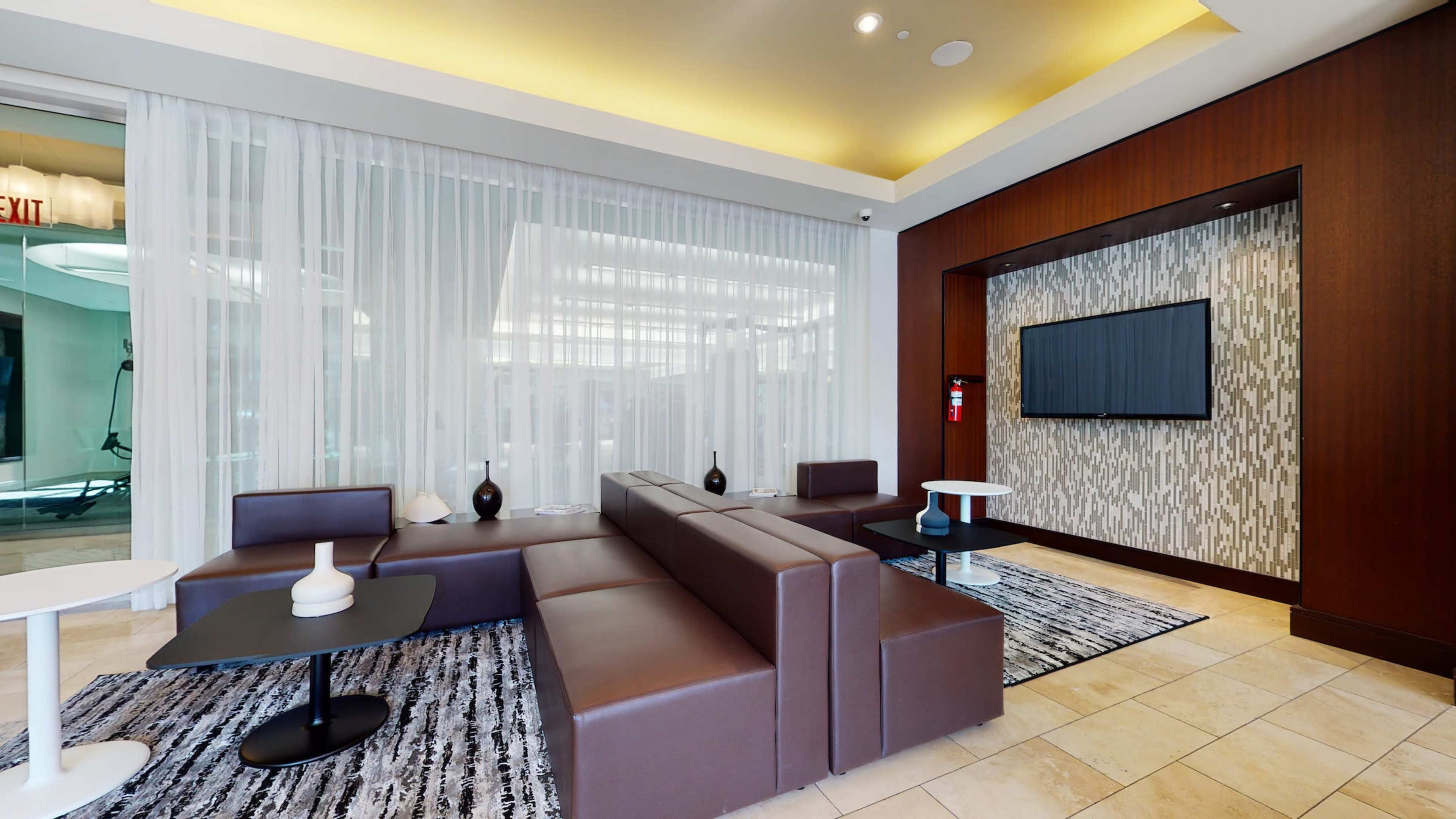 A modern lounge area featuring brown leather seating, white tables, and a television mounted on a wall with decorative paneling.