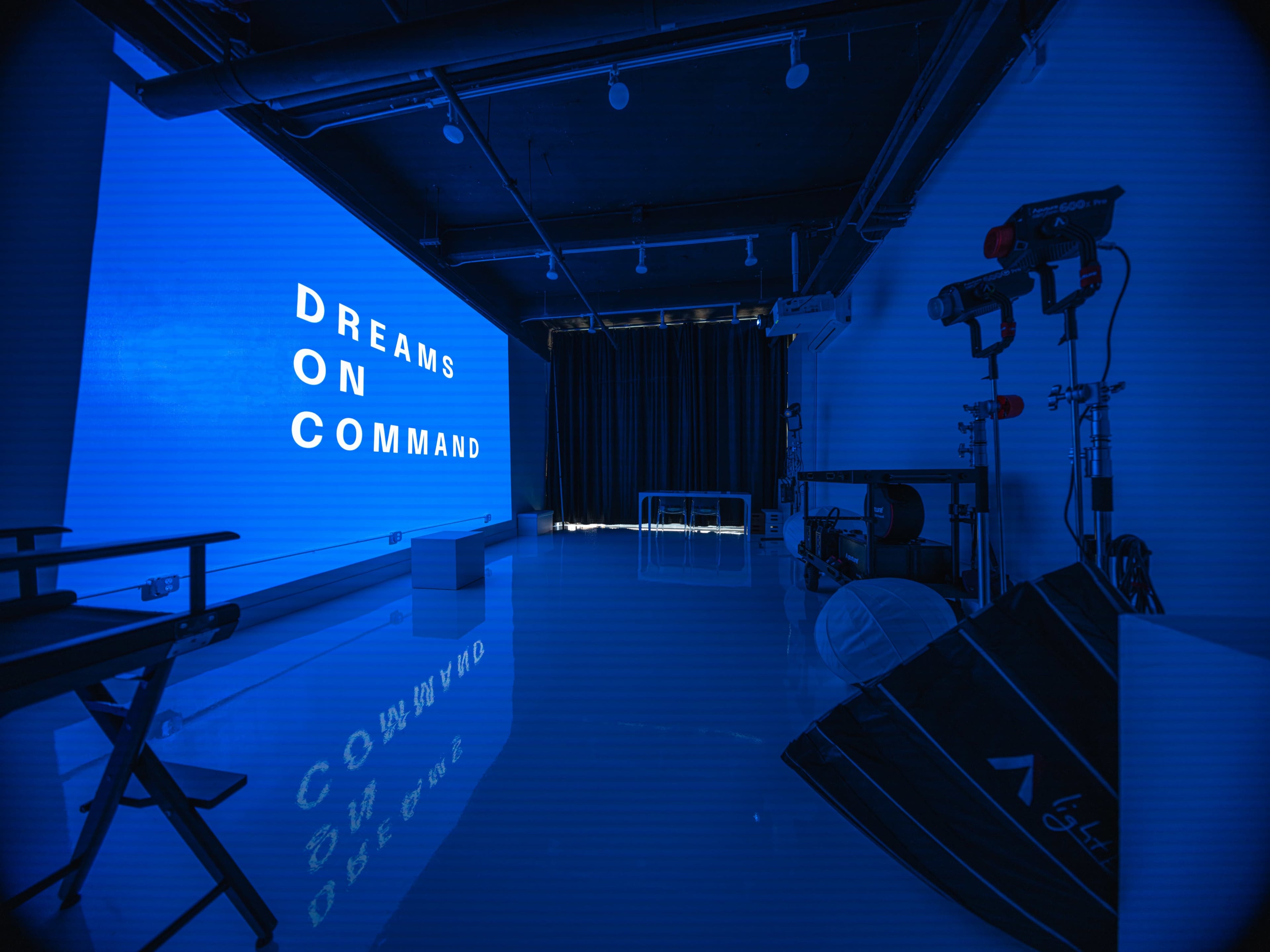 A modern studio space with a blue wall displaying the words "DREAMS ON COMMAND," and various photography equipment arranged in the room.