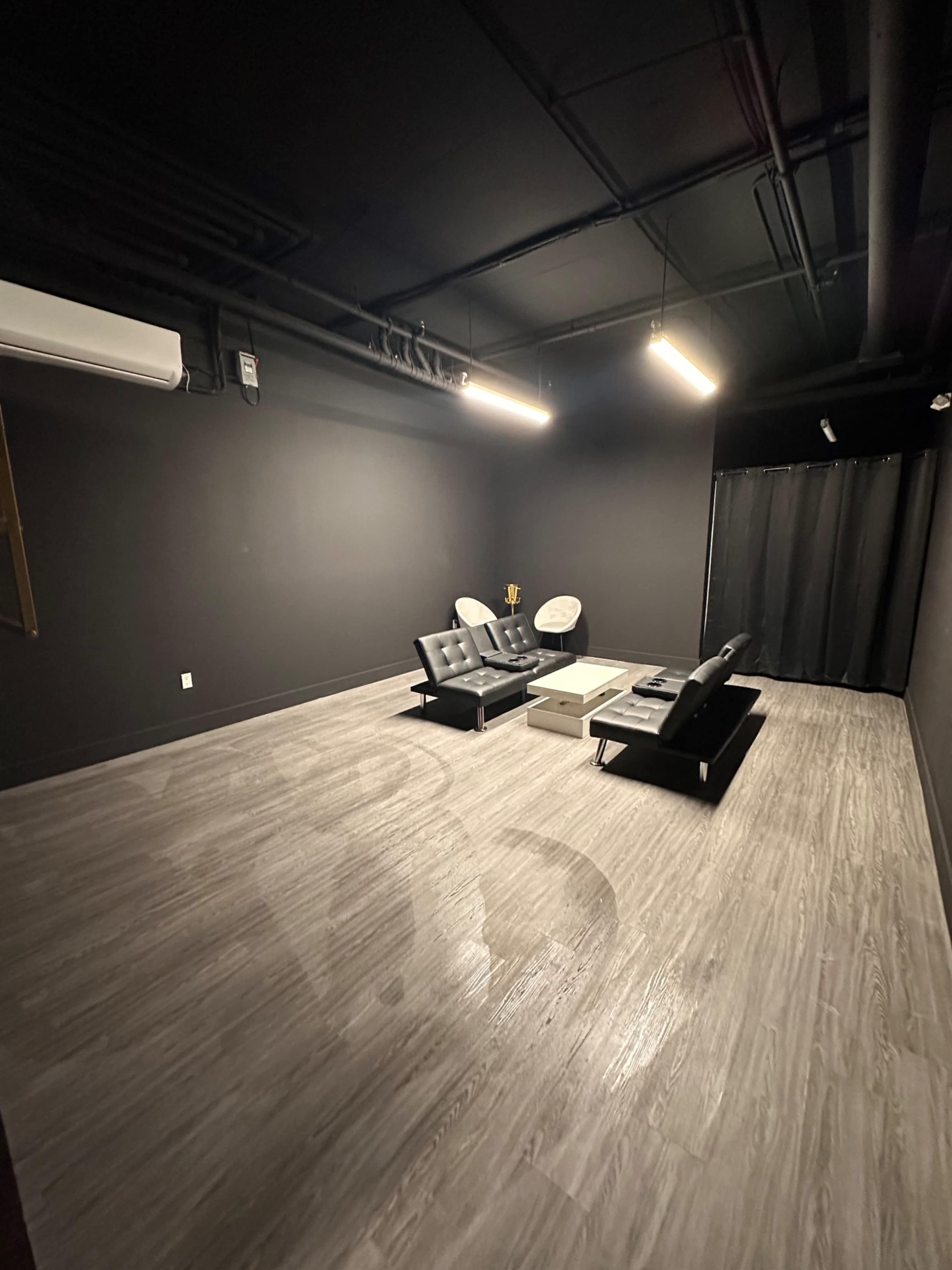 A sparsely furnished black-walled room featuring two couches, a coffee table, and a curtain in one corner.