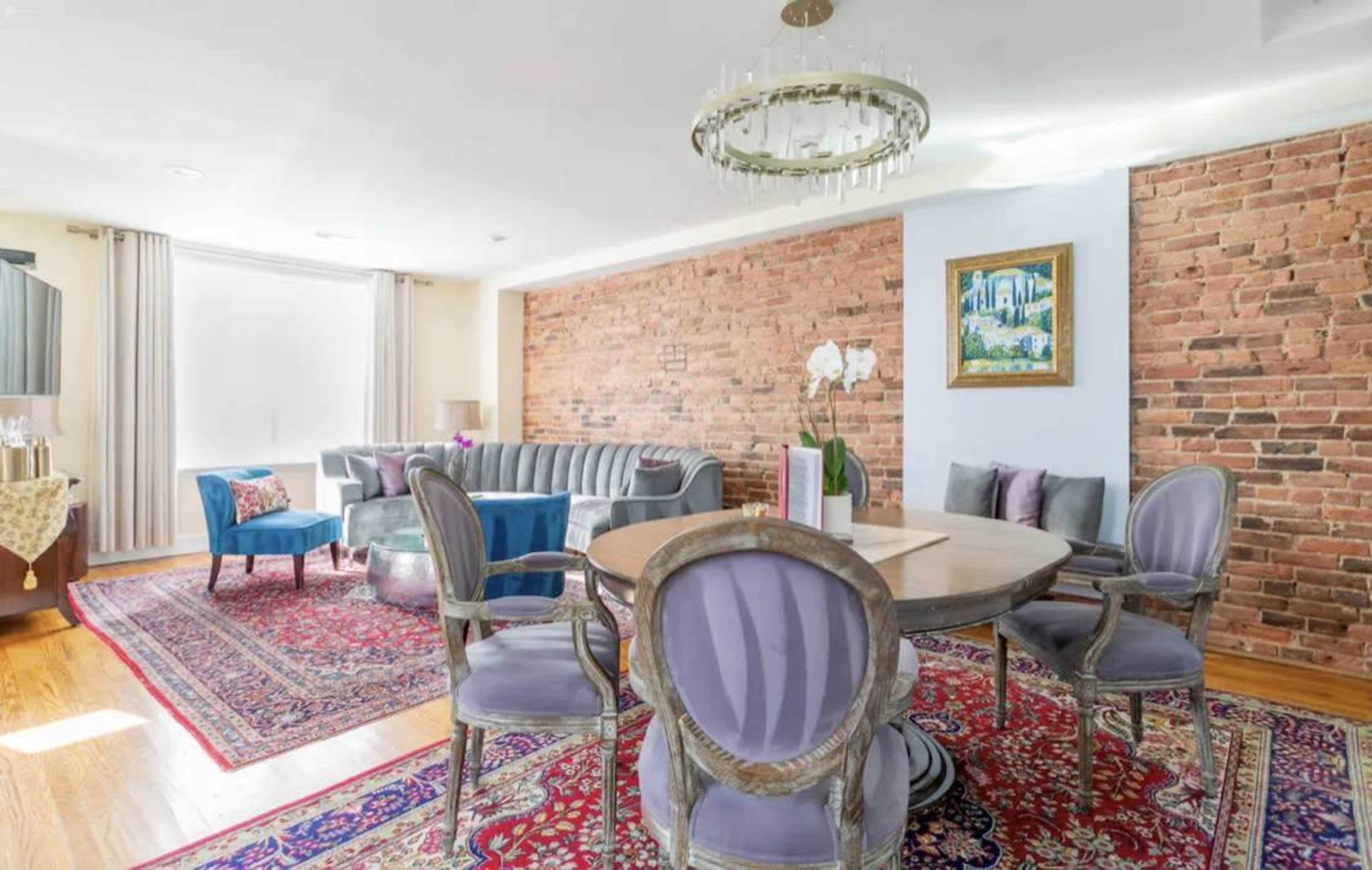 A modern living space with a dining area, showcasing a round table surrounded by ornate chairs, a striped couch, and a brick accent wall.