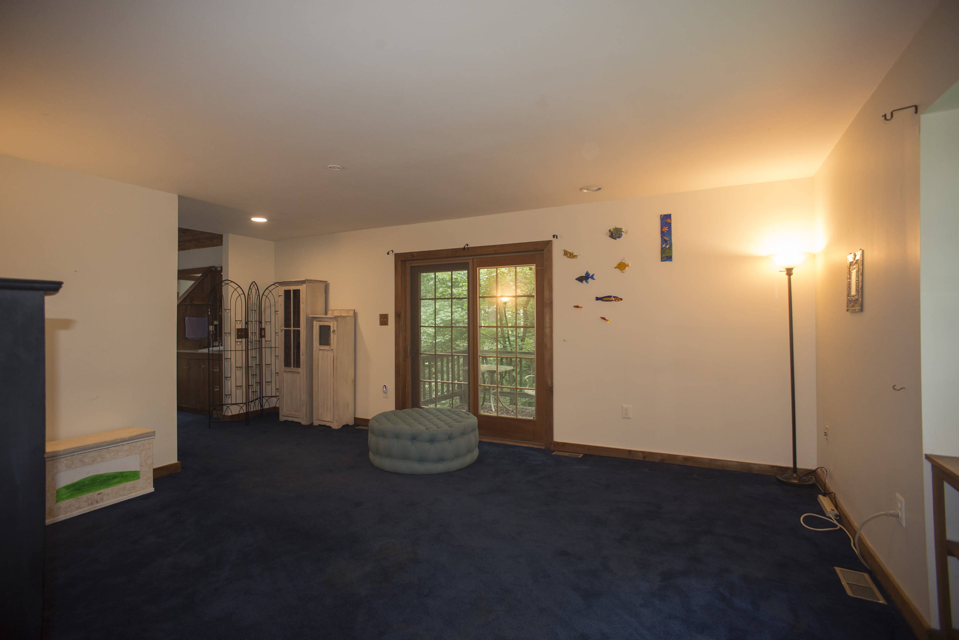 An empty room with blue carpet, a teal pouf, and a door with windows leading outside.