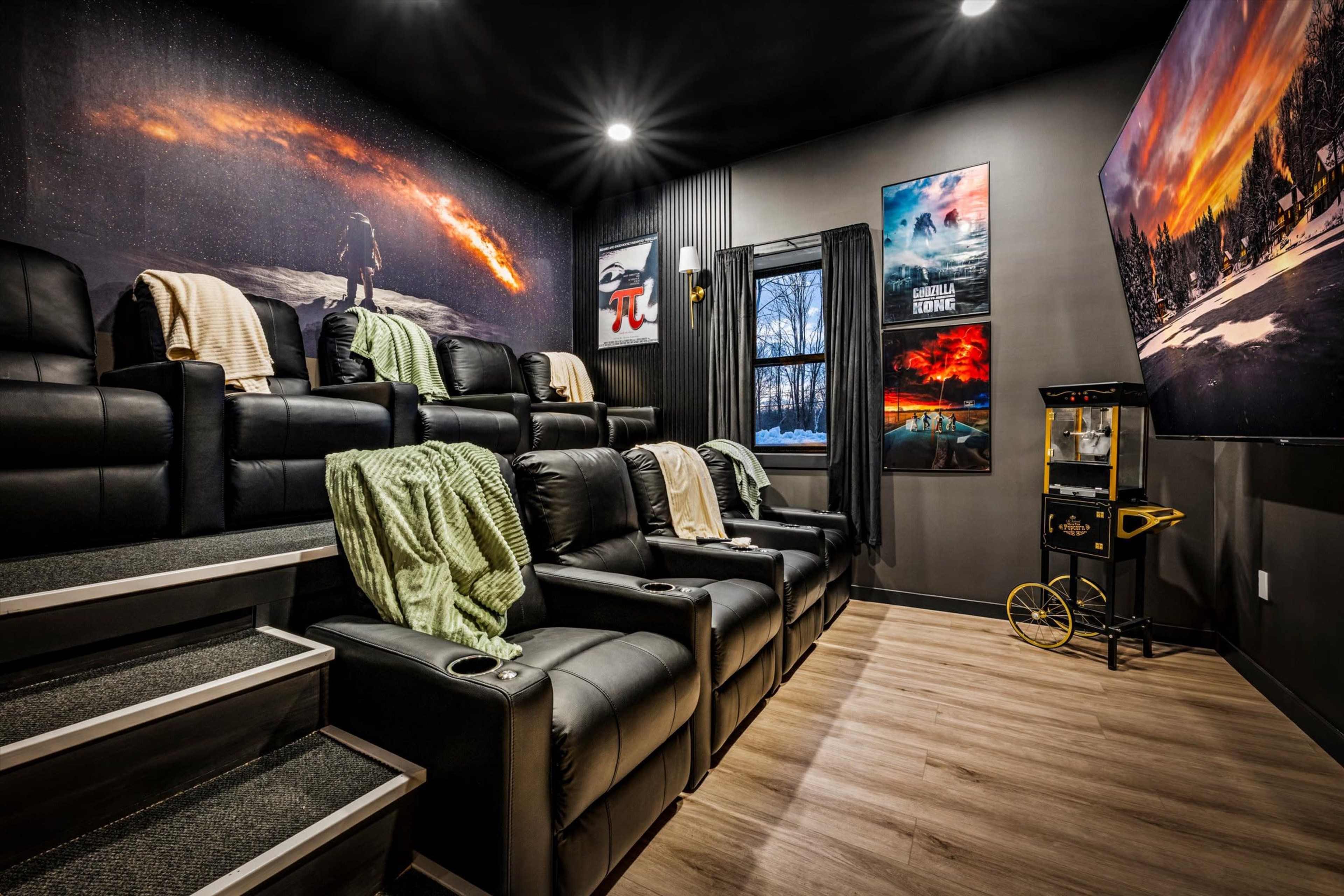 The image shows a home theater room featuring black reclining chairs arranged on a stepped platform, with blankets draped over them and movie posters on the walls.