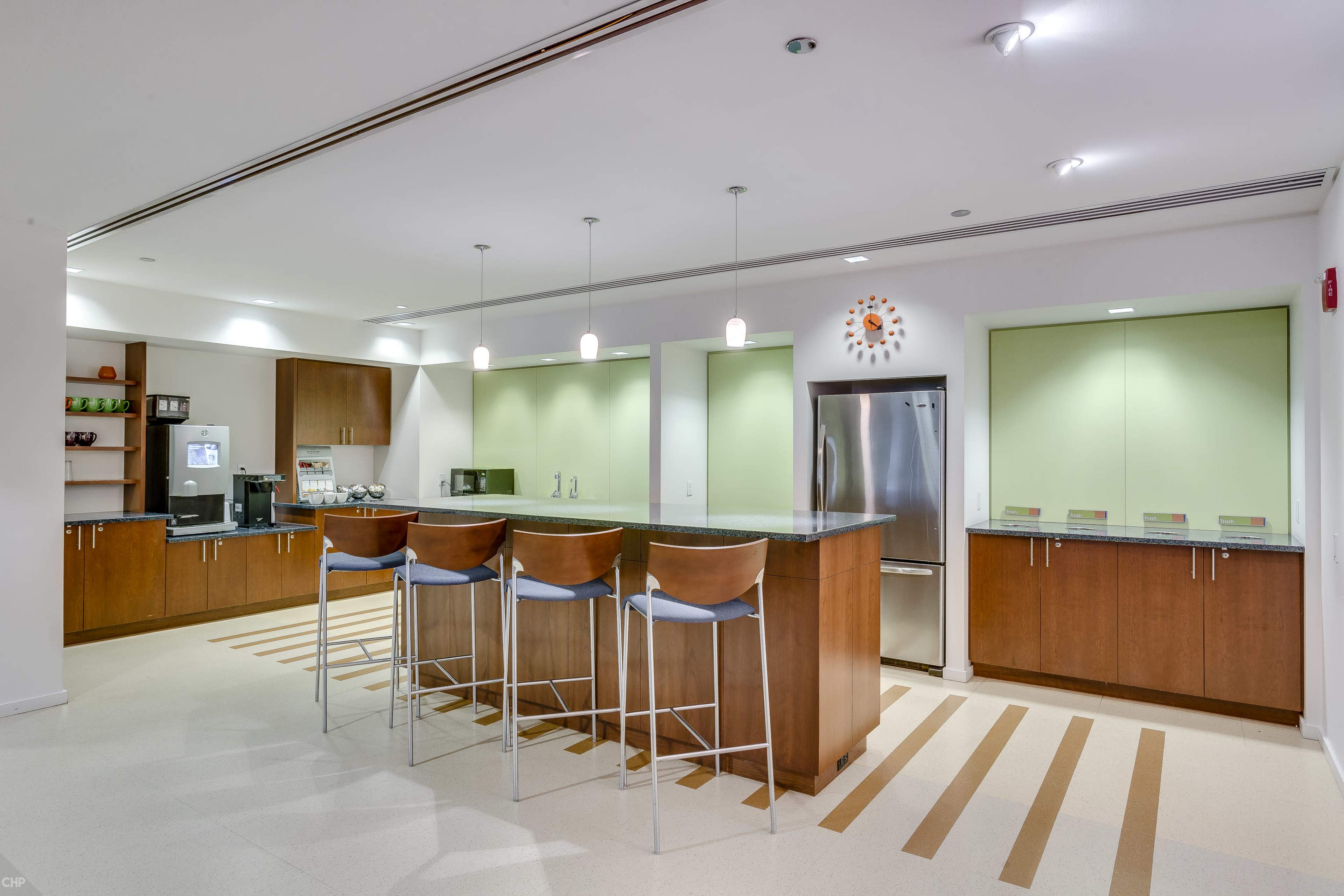 A modern kitchen features a long island with four stools, stainless steel appliances, and light green cabinetry.