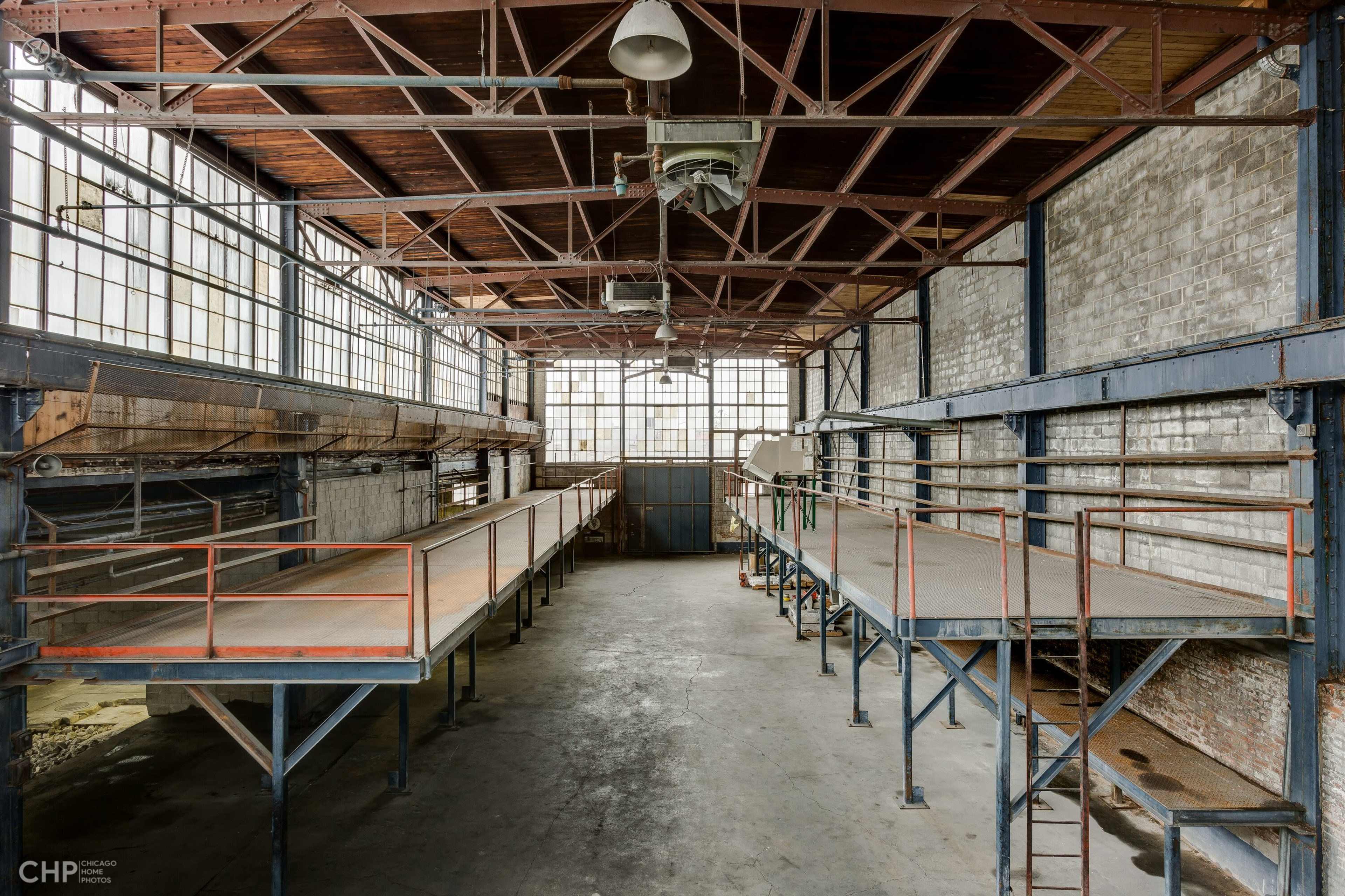 An empty industrial warehouse with high ceilings, large windows, and elevated platforms along the walls.