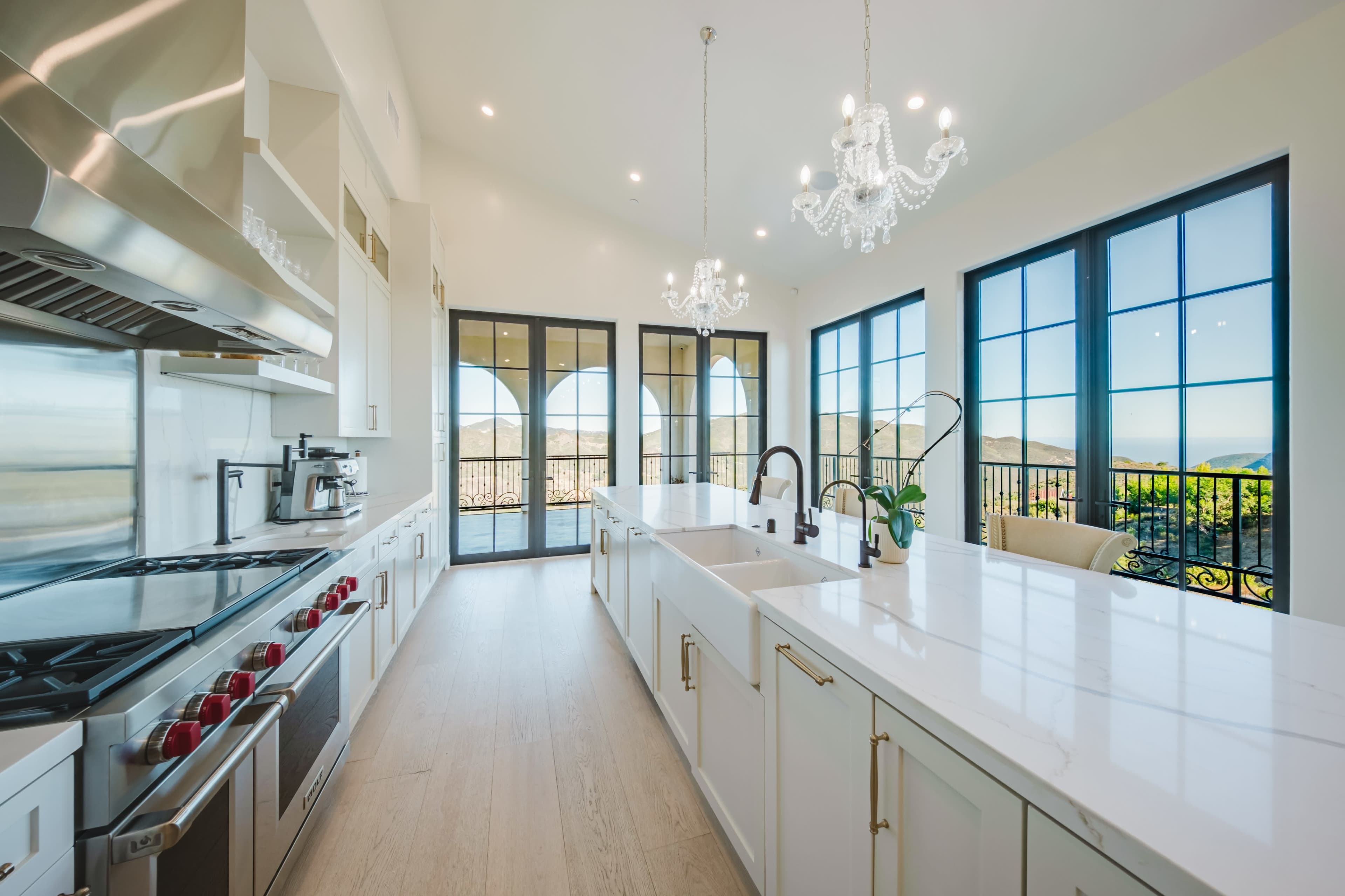 A modern kitchen features stainless steel appliances, white cabinetry, and large windows with mountain views.