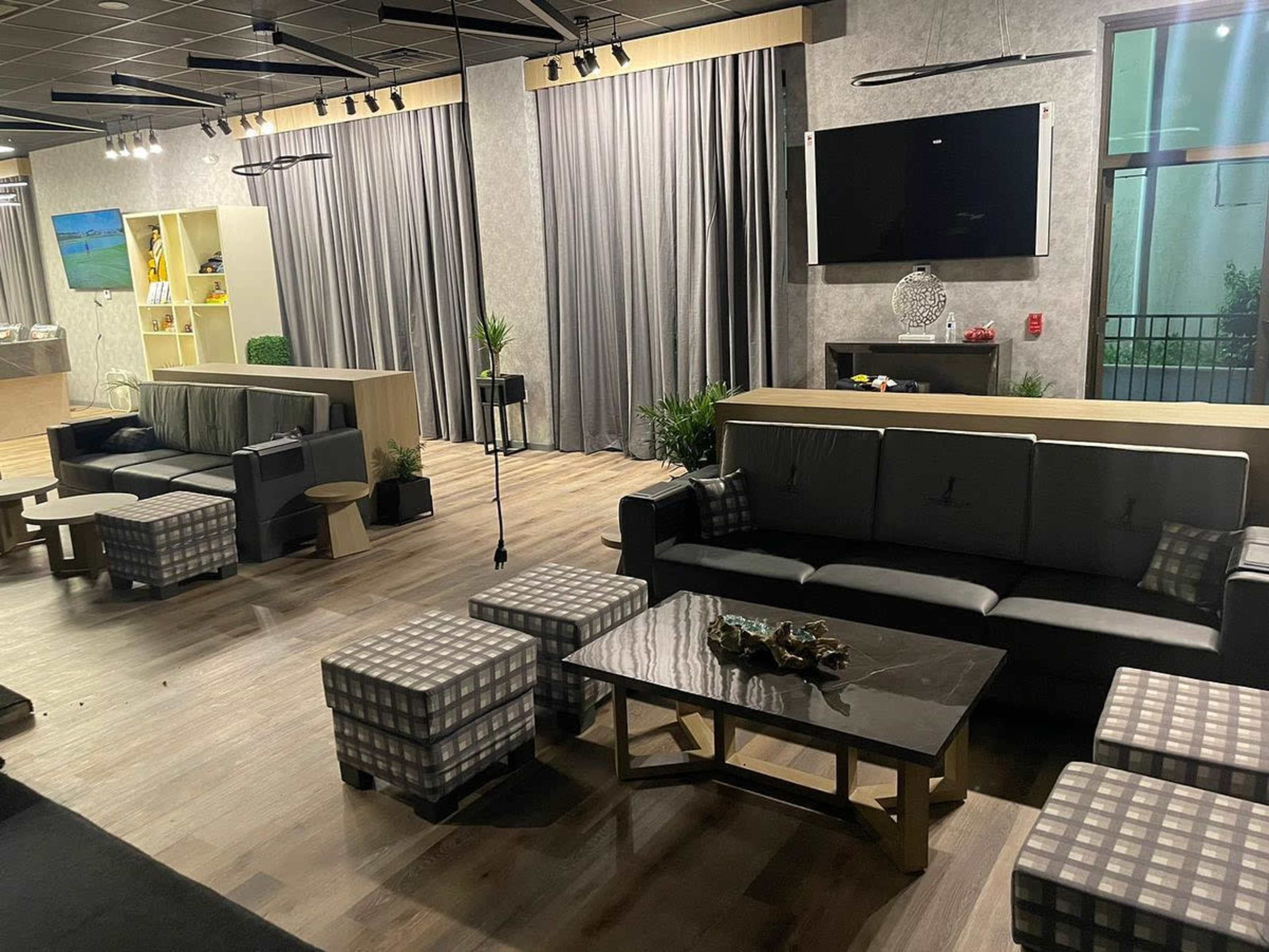 A spacious lounge area with gray curtains, modern sofas, and several squared stools arranged around a central coffee table.