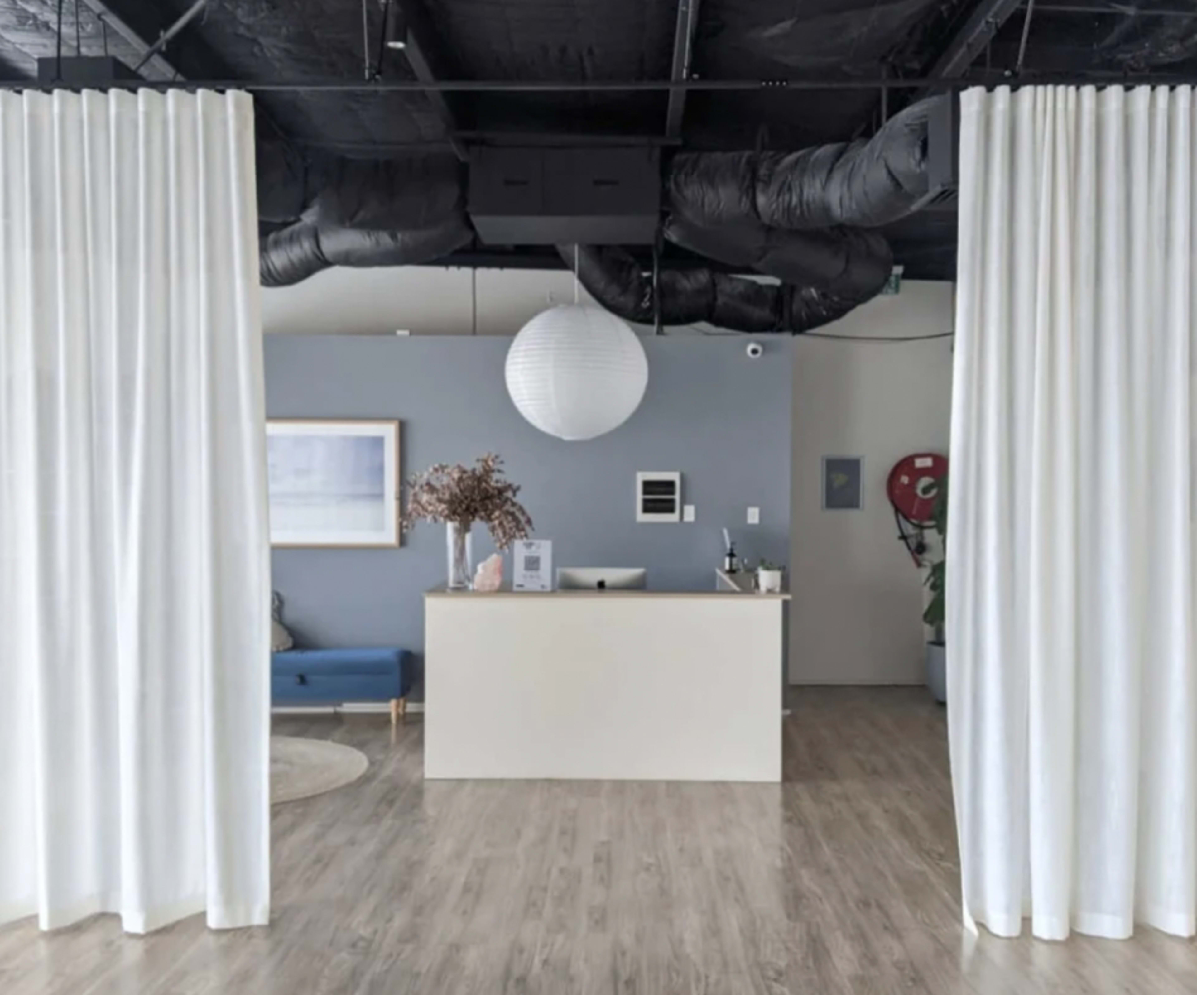 A modern reception area with a white countertop, a blue couch, and sheer white curtains separating the space.