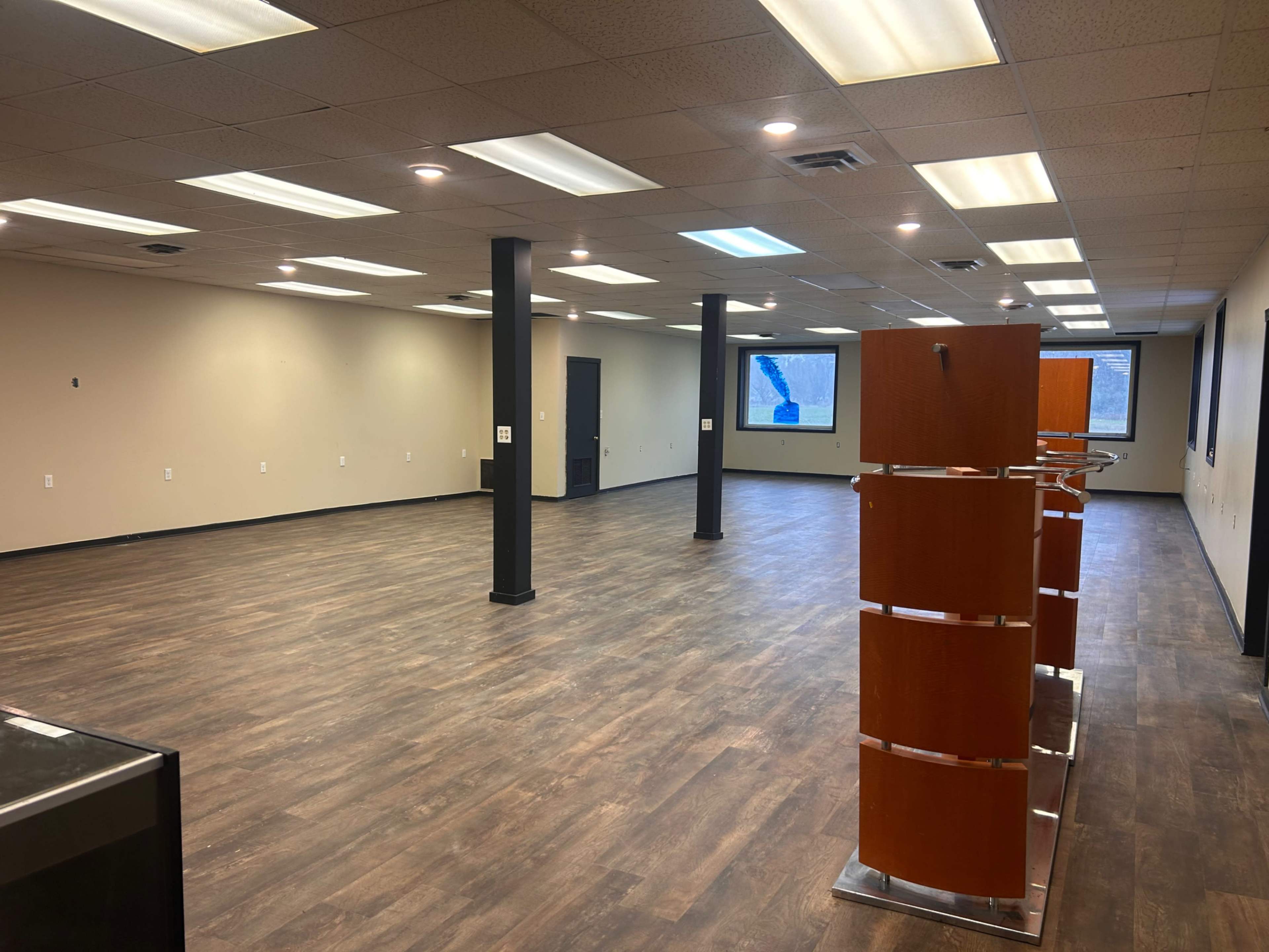 The image shows a large, empty commercial space with wooden flooring, gray walls, and a few display stands.