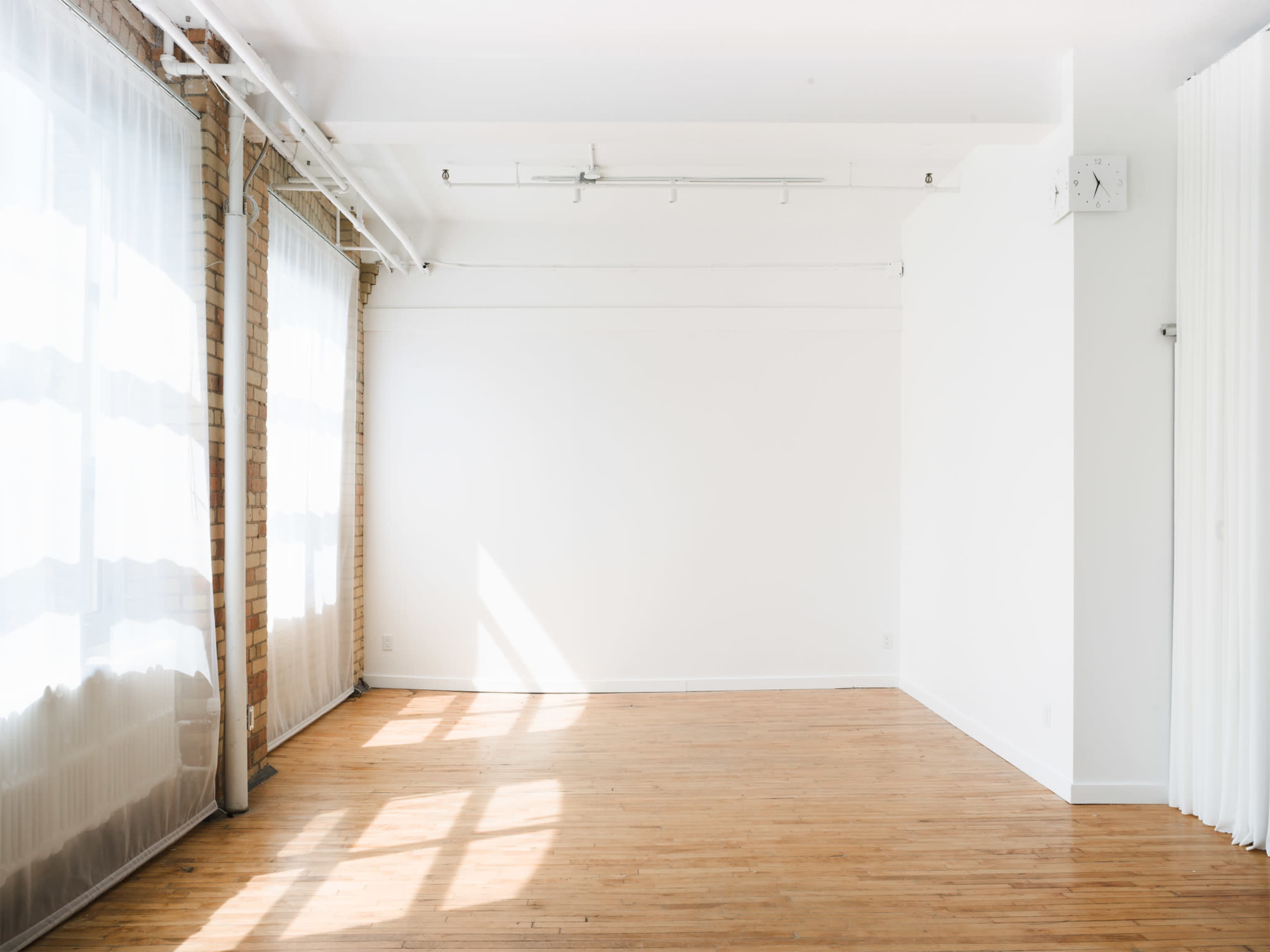 The image shows a spacious, bright room with large windows allowing natural light to stream in, and light-colored wooden flooring.