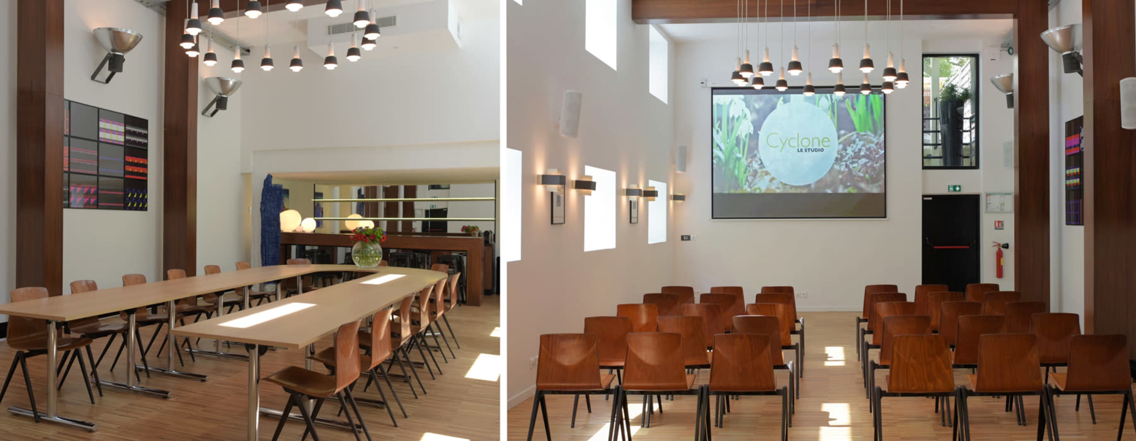 A modern meeting room featuring a long table on one side and rows of chairs facing a projection screen on the other side.