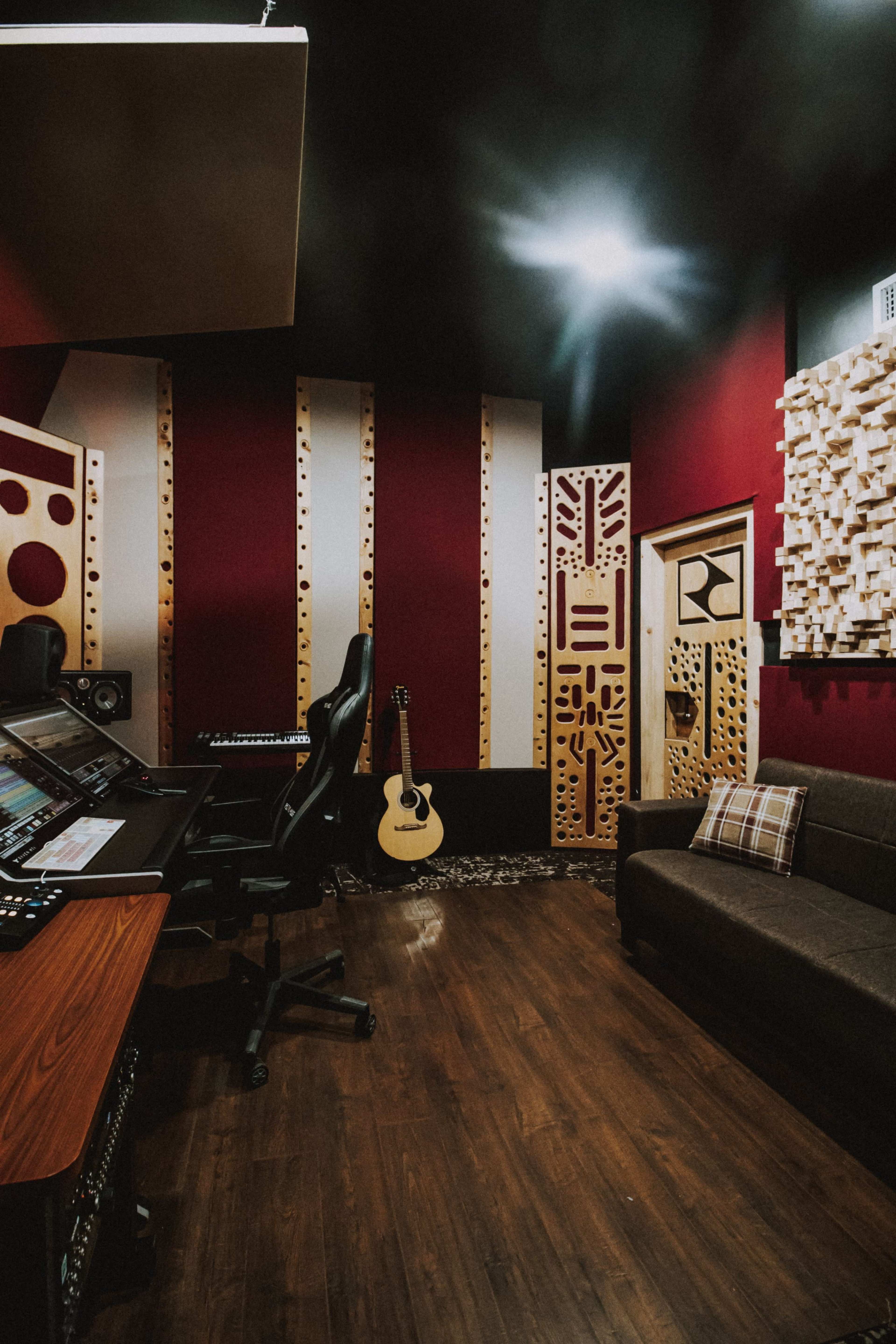 A music studio featuring a mixing console, a guitar leaning against the wall, and soundproofing panels on the walls.