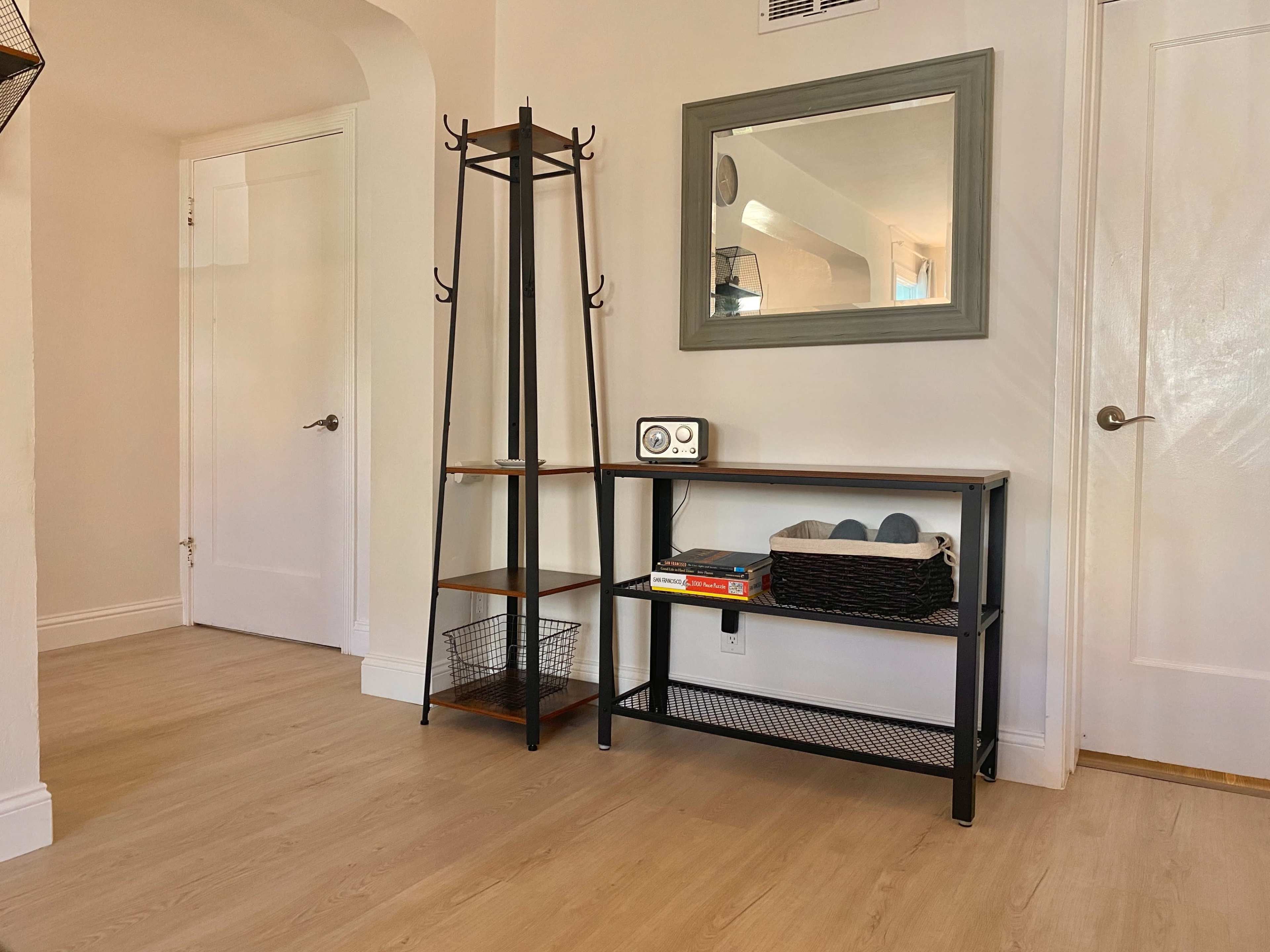 A small entryway with a metal and wood coat rack, a console table with a decorative basket and books, and a mirror on the wall.