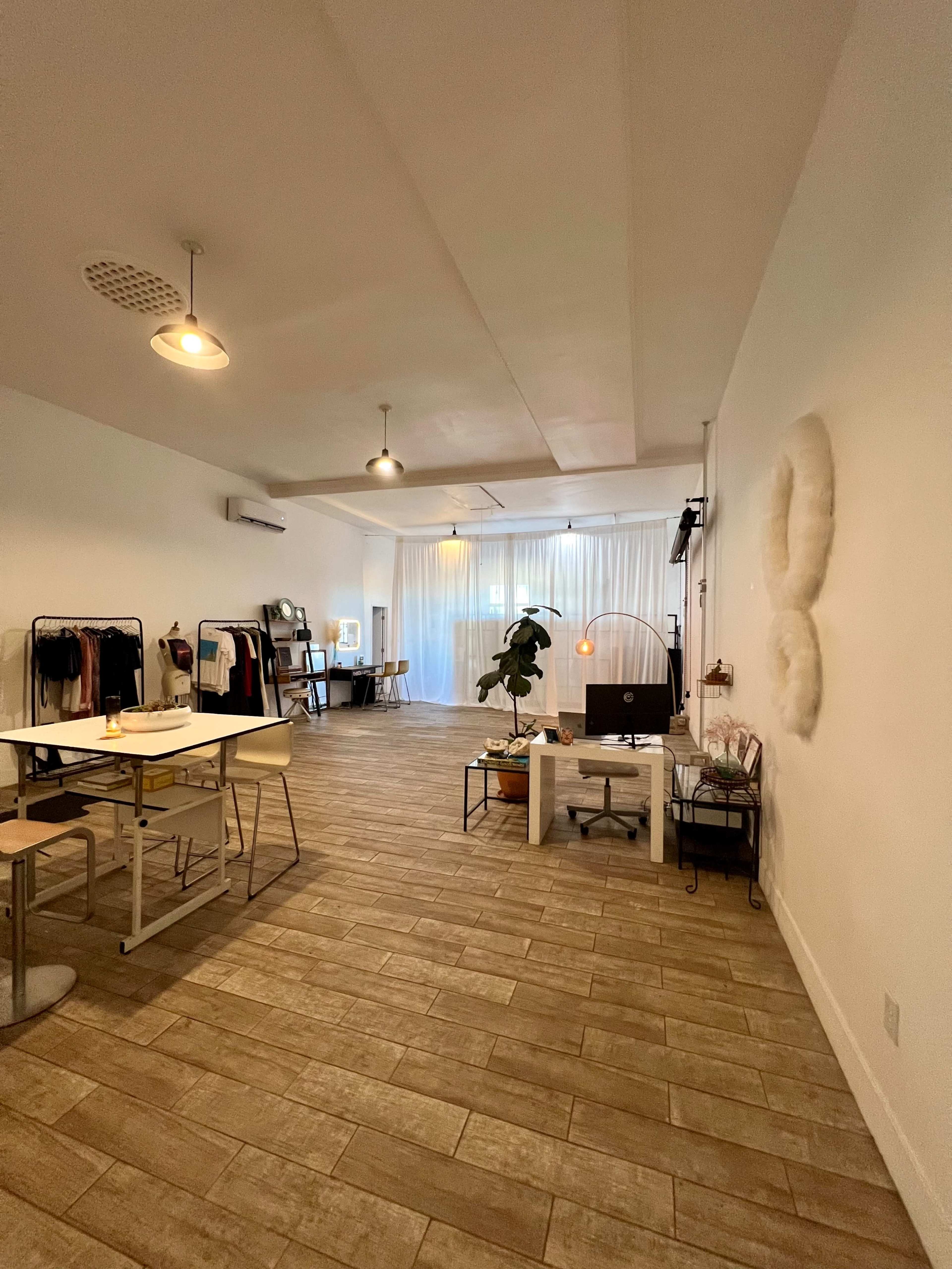 A spacious, well-lit studio with clothing racks, a table with chairs, and a soft white curtain in the background.