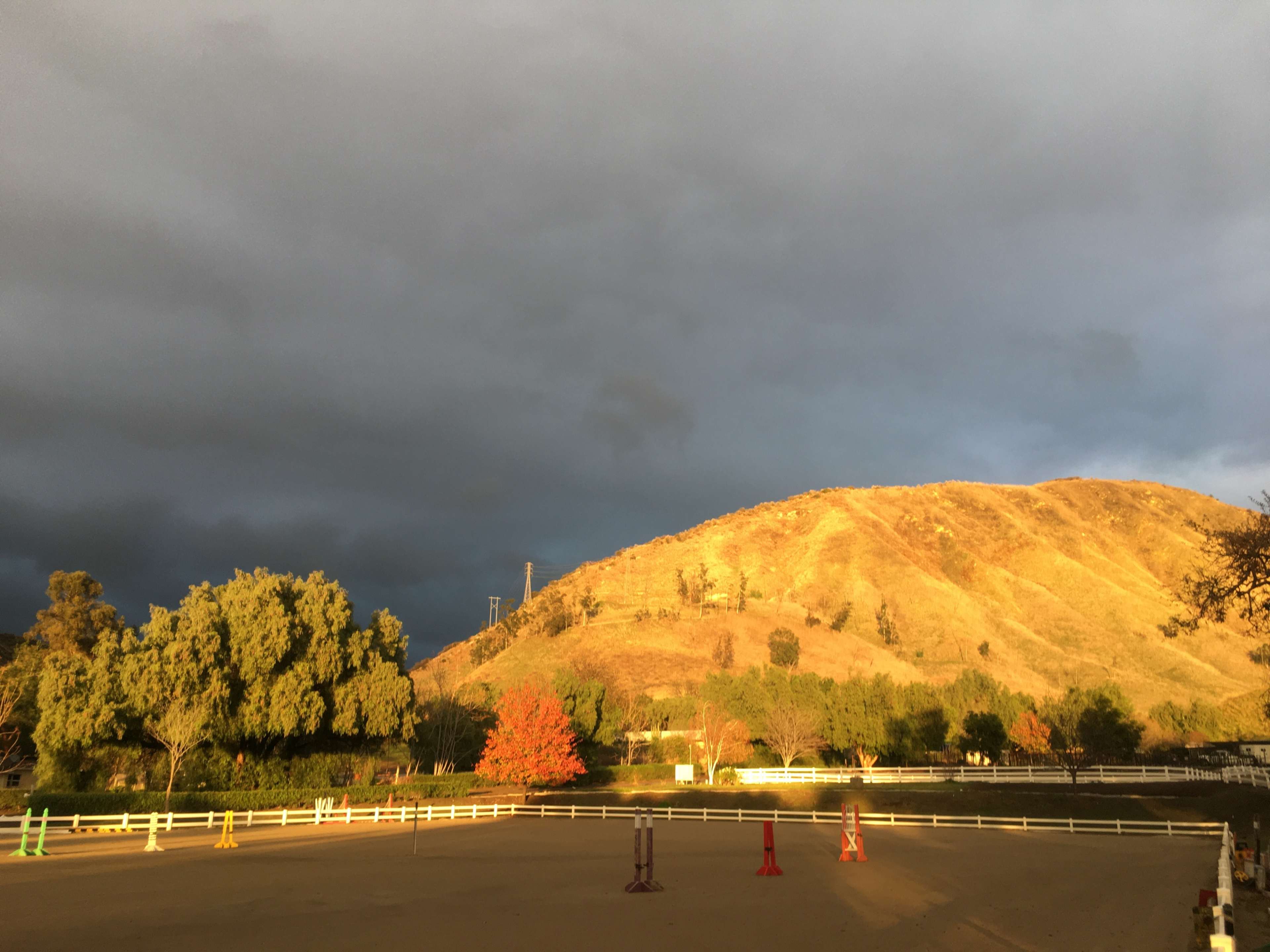 An equestrian arena with a warm-lit hillside and dark clouds above.