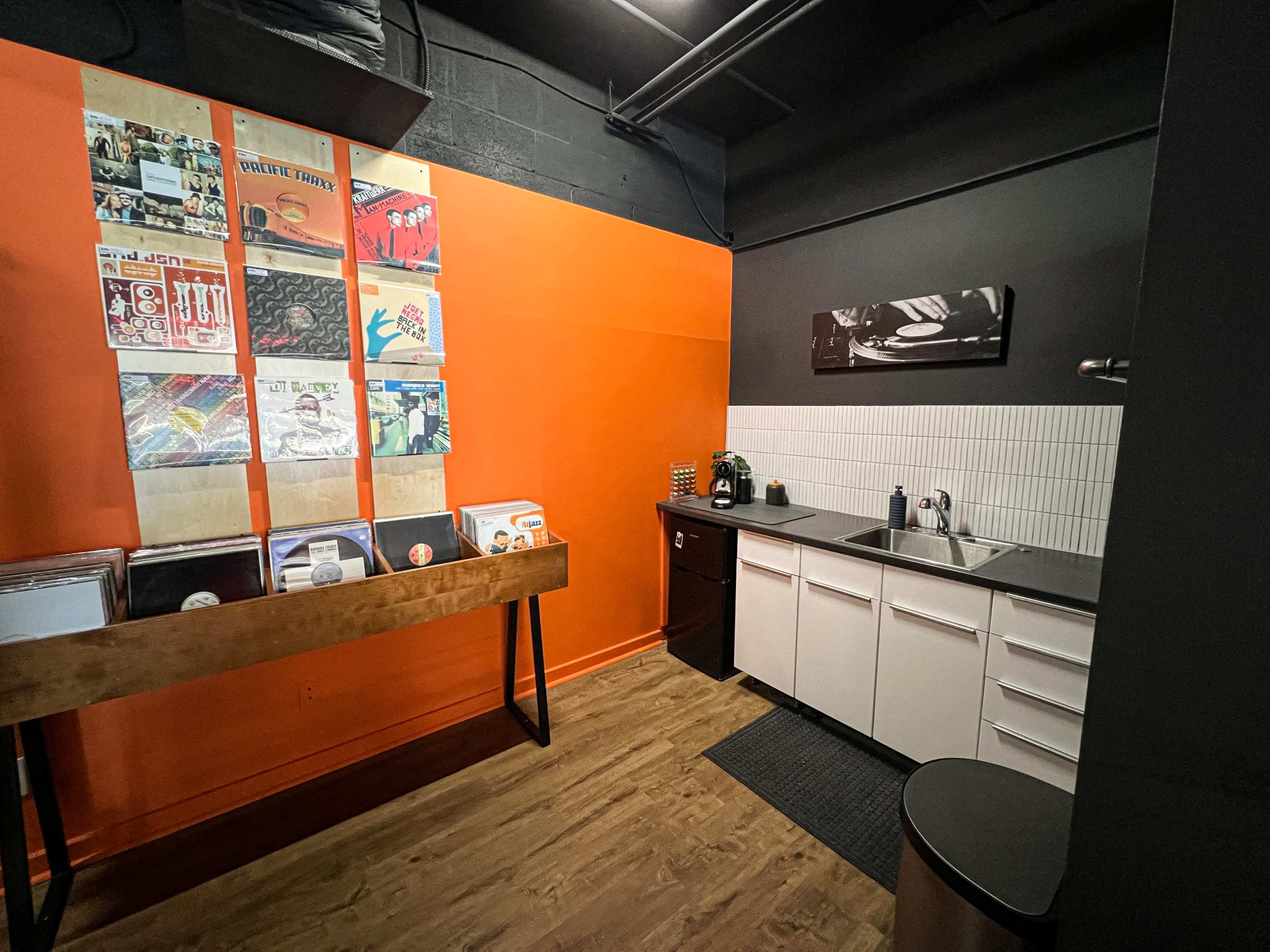 A small kitchen area with a black and orange wall, a countertop with a sink, and a display of vinyl records on a wooden shelf.