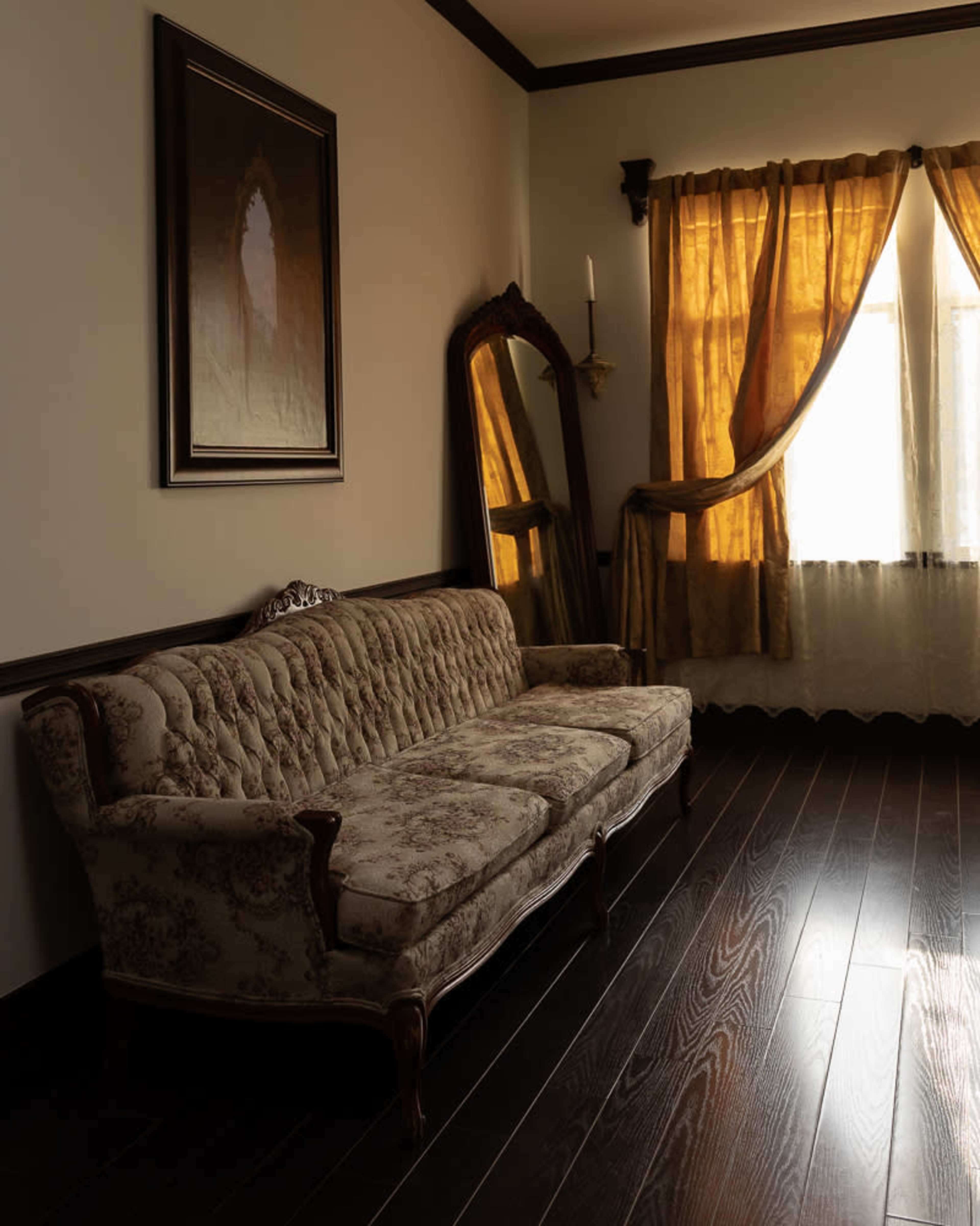 The image features a vintage sofa in a room with warm sunlight streaming through sheer curtains and a large mirror reflecting the space.