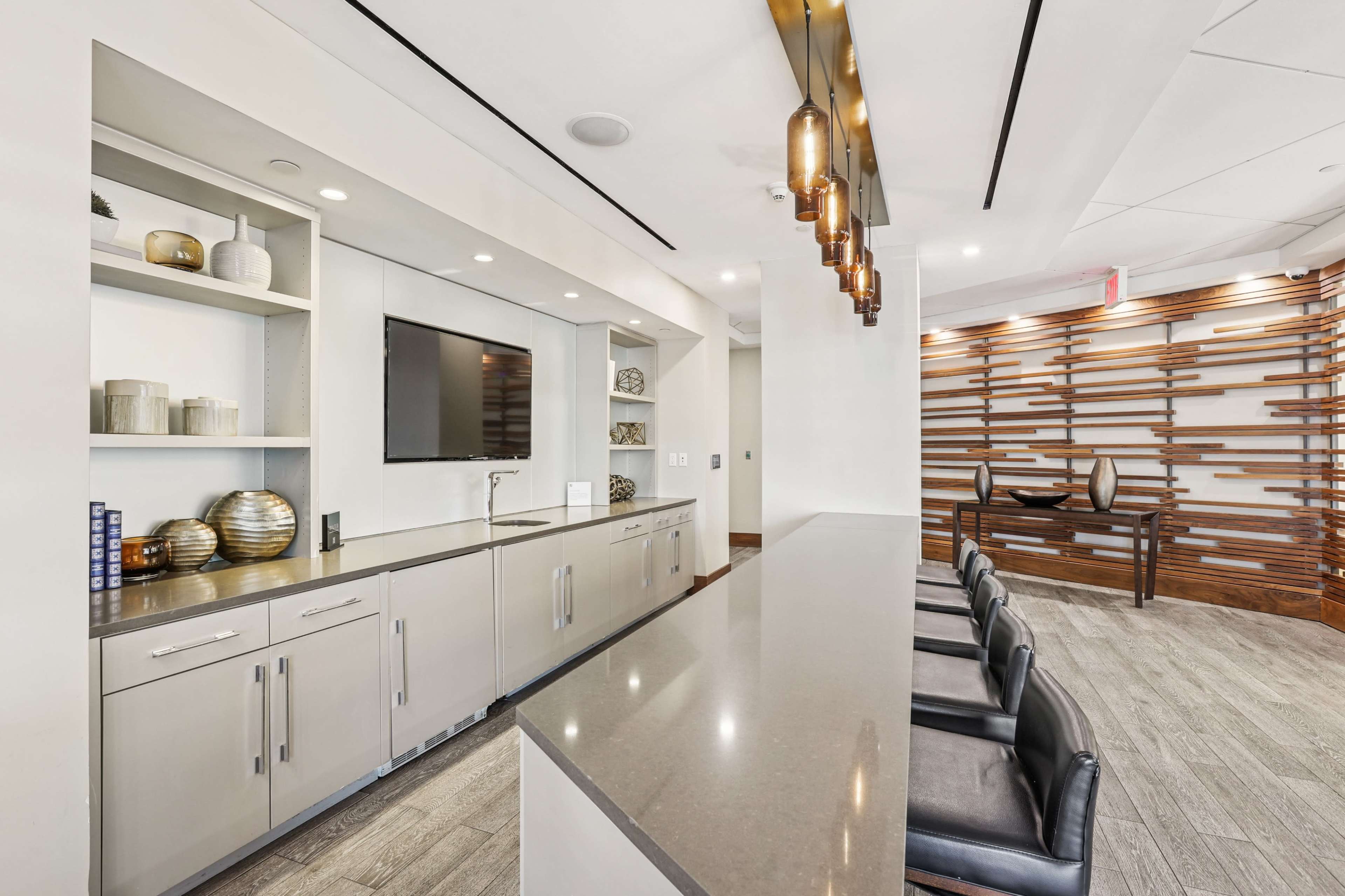 The image shows a modern kitchen or lounge area with a sleek countertop, storage cabinetry, and stylish lighting fixtures.
