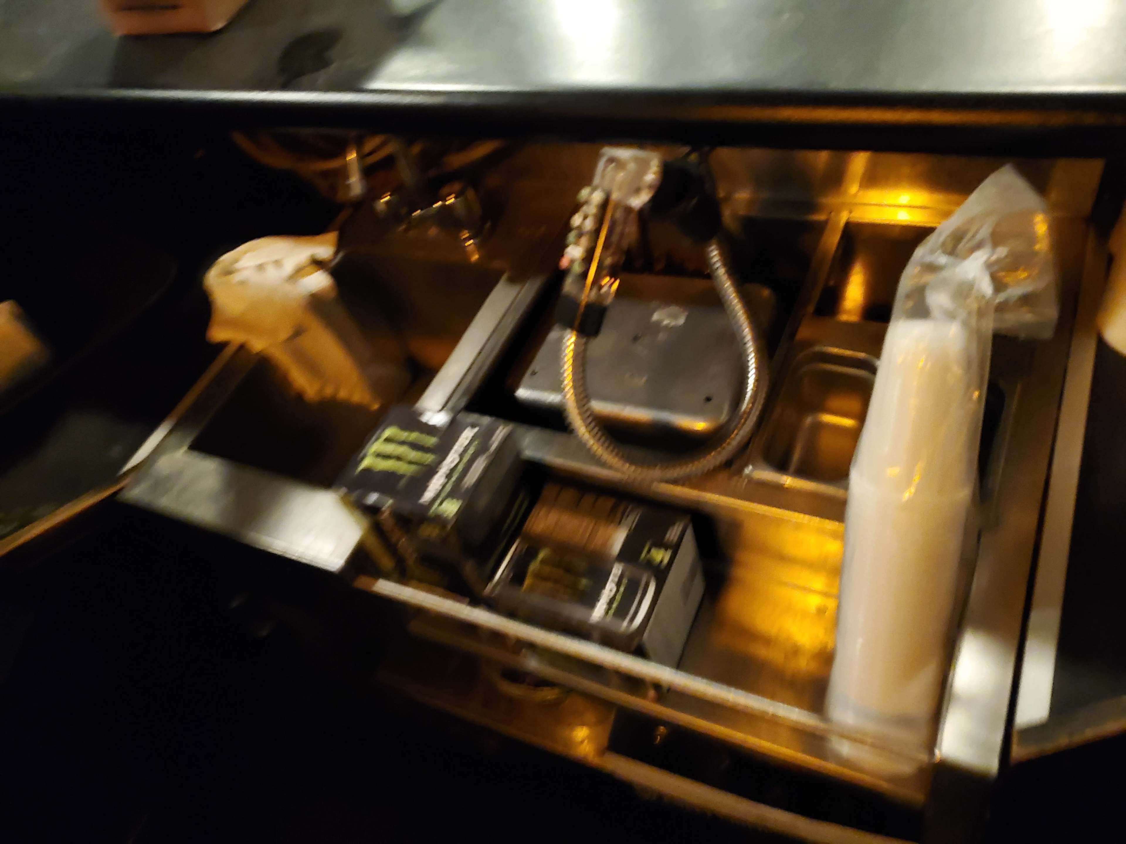 The image shows a dimly lit countertop with a sink, a faucet, and several boxes of Monster energy drinks.