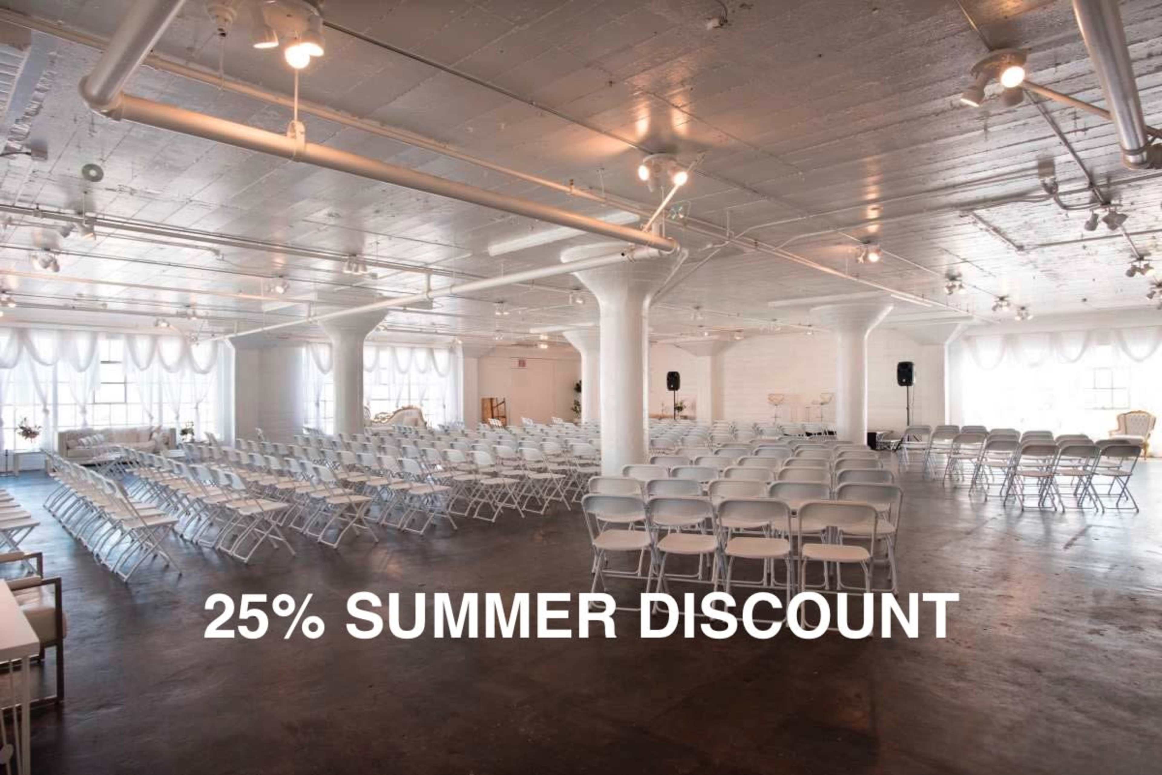 The image shows a spacious event hall set up with rows of white folding chairs and illuminated by overhead lights.