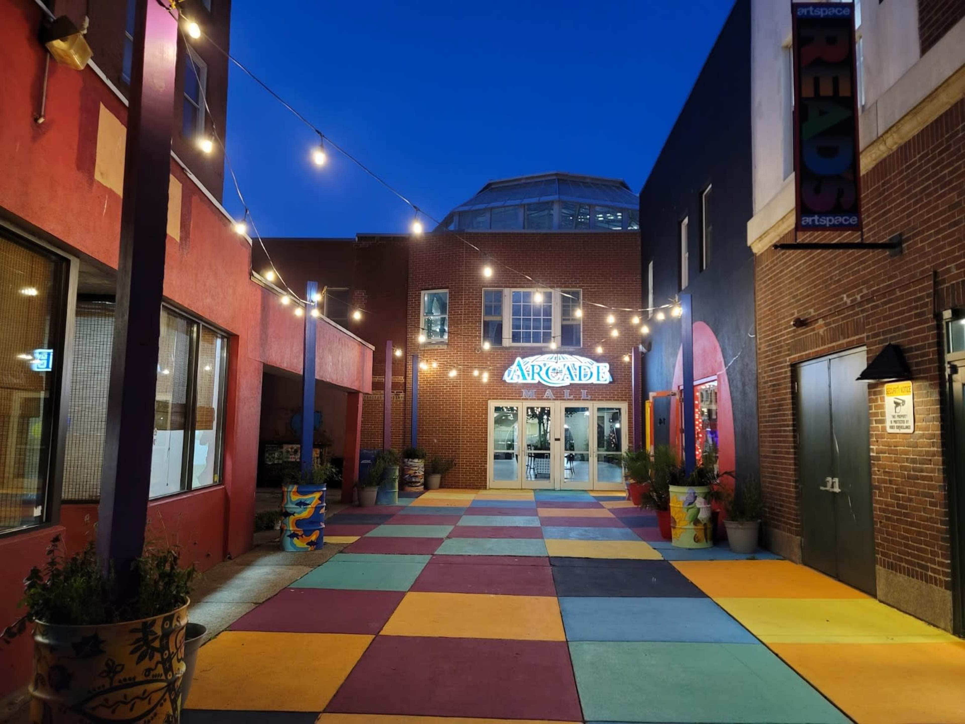 A vibrant courtyard with colorful tiles, string lights overhead, and an entrance labeled "ARCADE."