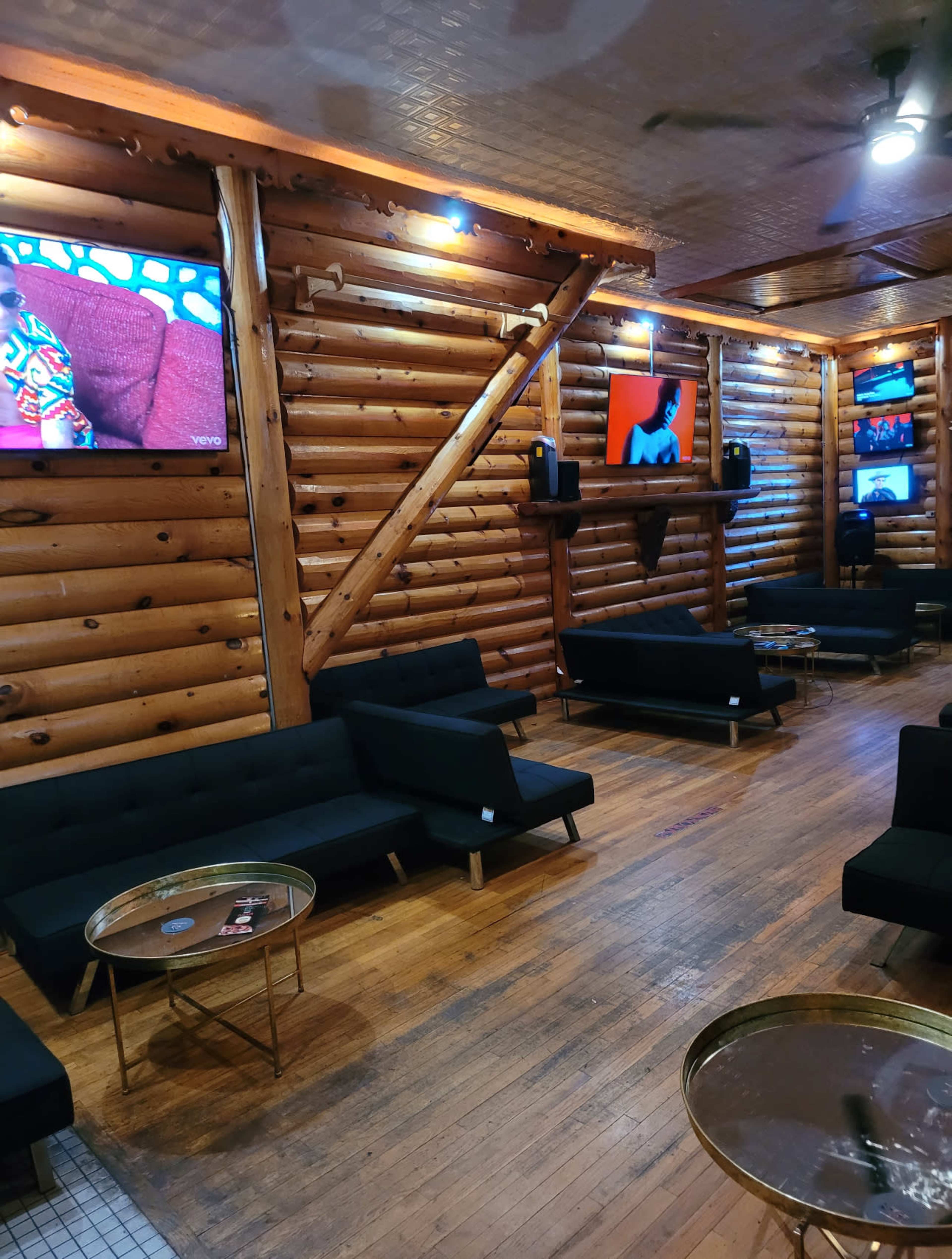 The interior features a cozy lounge with wooden walls, black couches, and several televisions mounted on the walls.