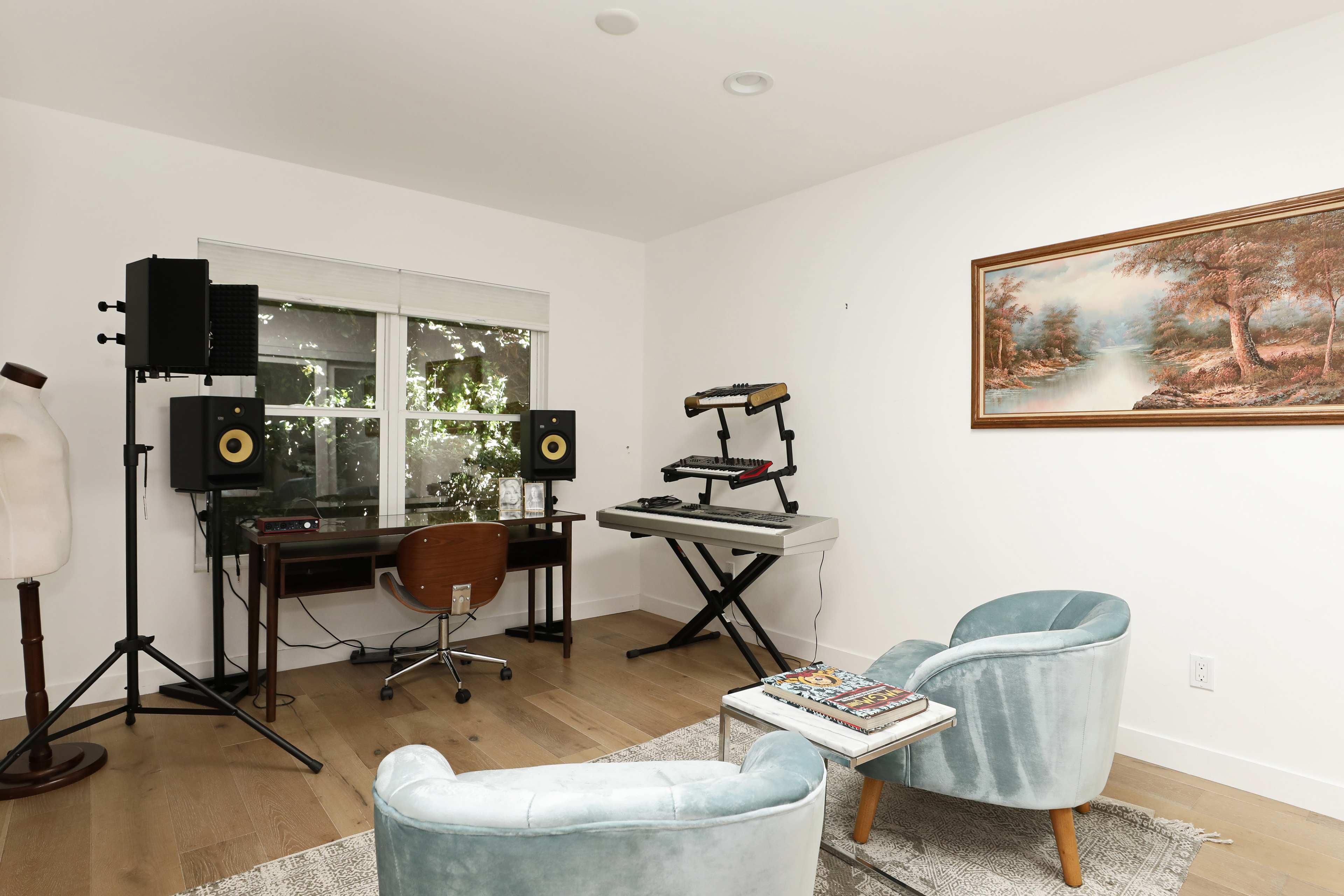 A modern workspace features a desk with a keyboard and speakers, framed by two blue chairs and a window.