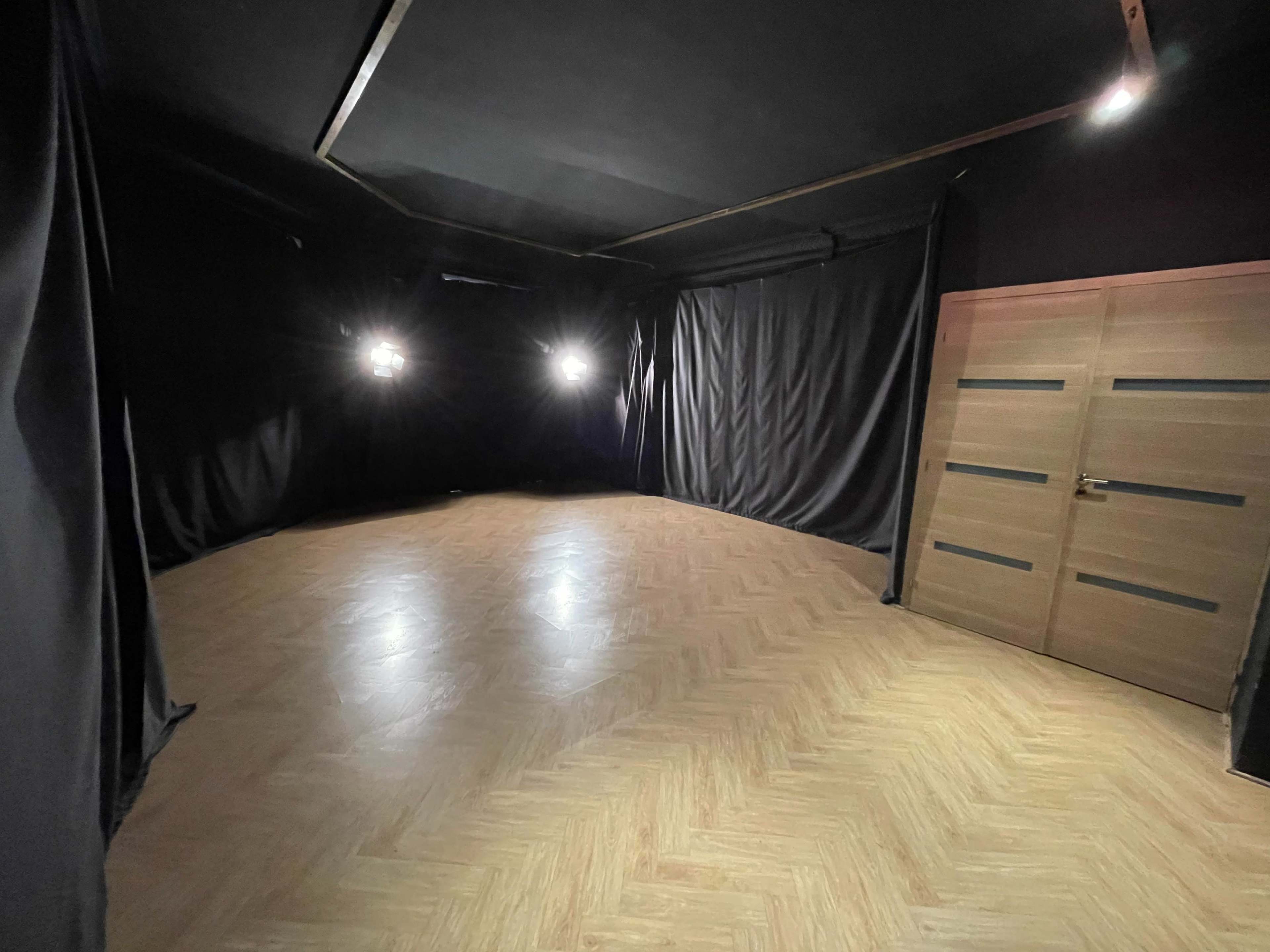 A dimly lit room with black curtains on the walls and a wooden door on one side.
