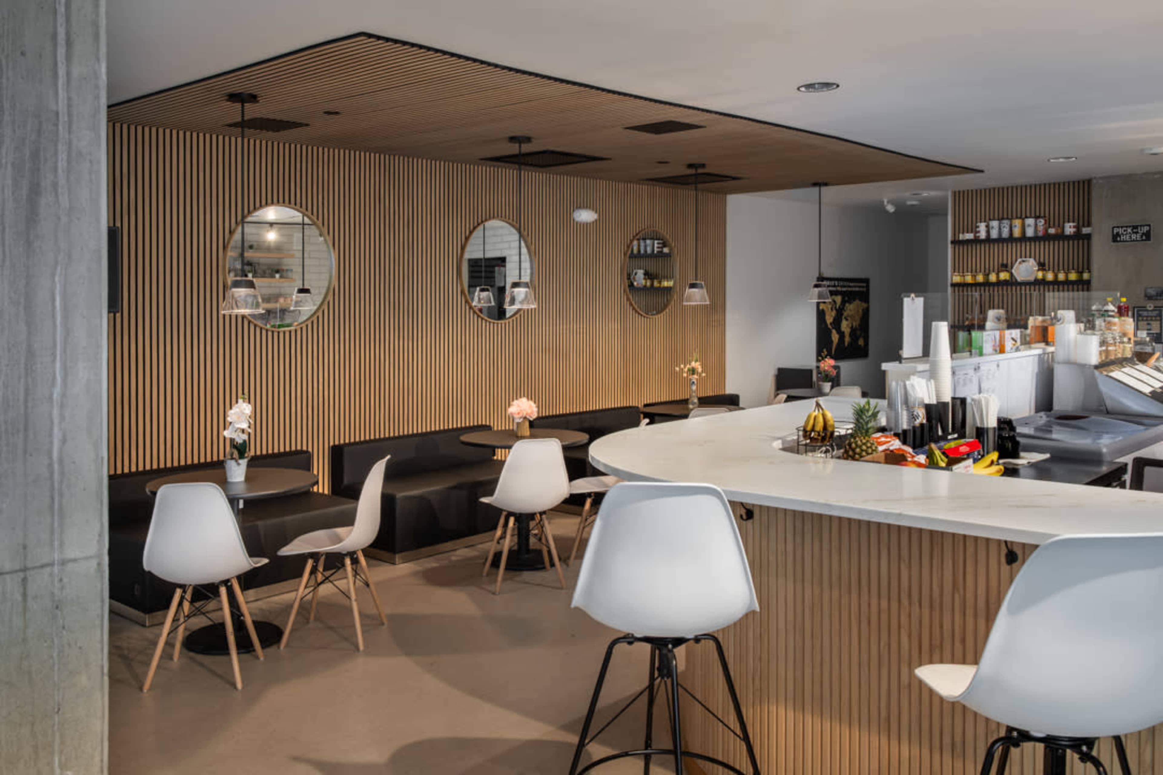 The image shows a modern cafe interior with wooden wall paneling, round mirrors, and a mix of white and black furniture, including a curved counter, tables, and chairs.