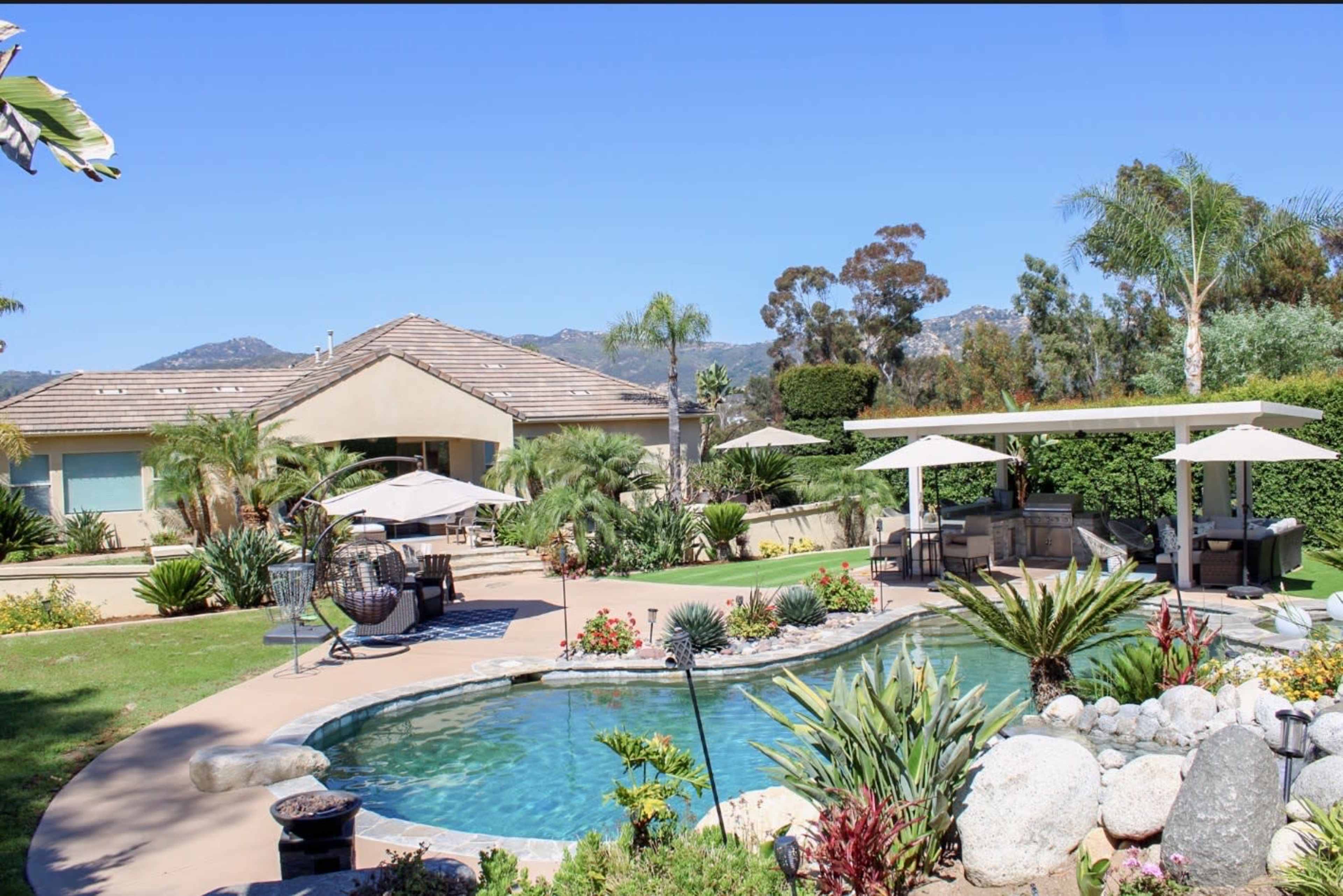 The image depicts a landscaped backyard with a swimming pool, palm trees, and a house in the background.