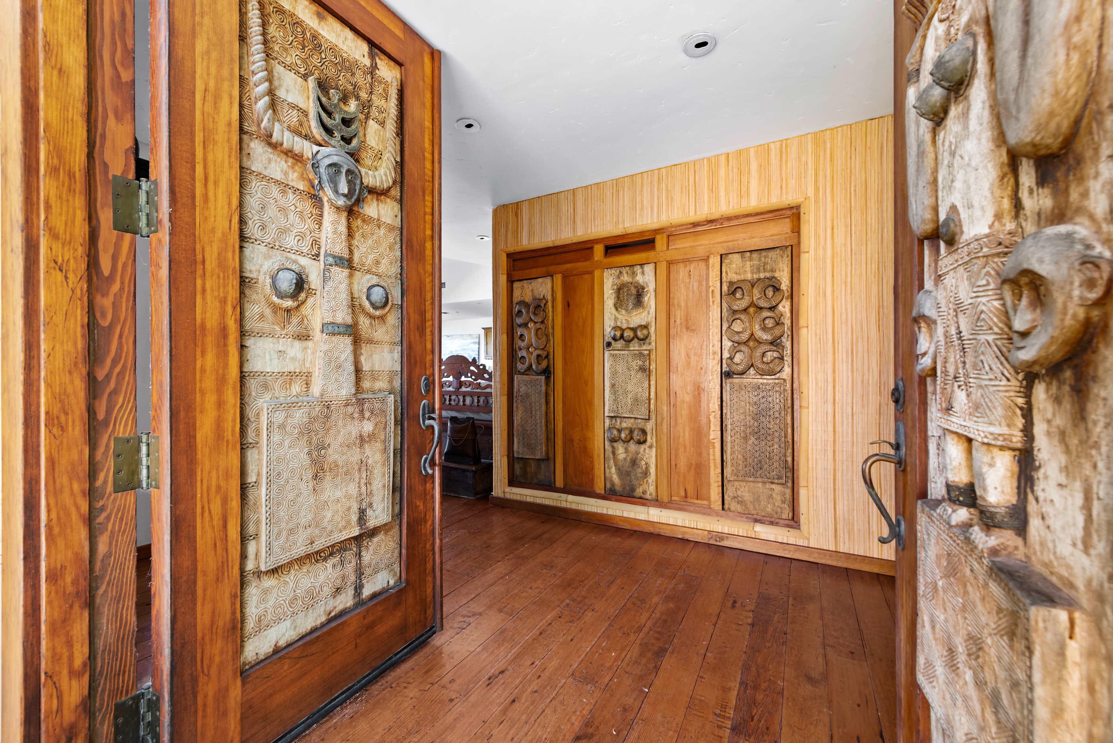 An entrance hallway featuring ornate wooden doors with intricate carving and textured wall panels in a warm-toned wooden setting.