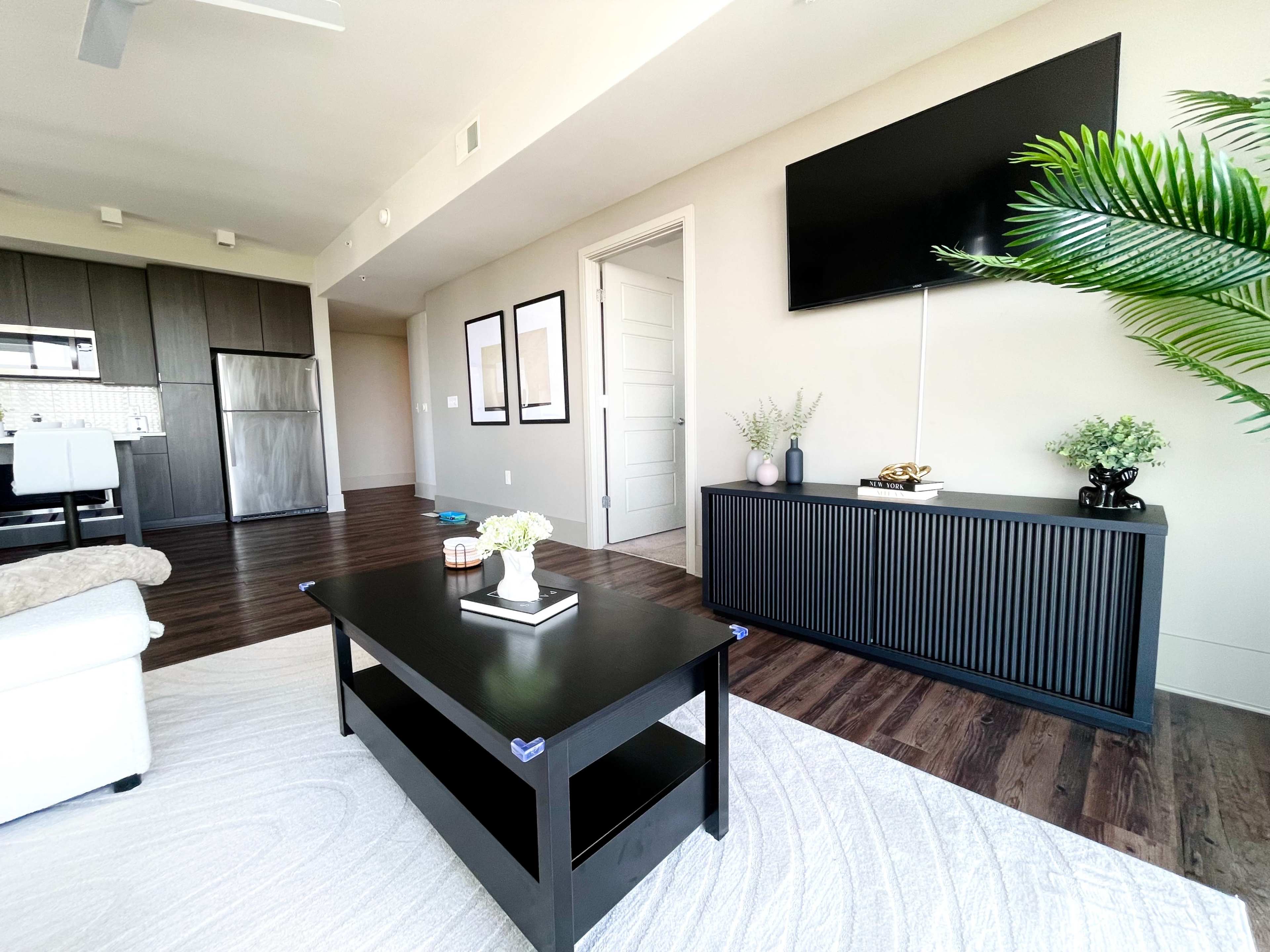 A modern living room with a black coffee table, a light-colored sofa, and a mounted flat-screen TV on a wall with a sideboard.