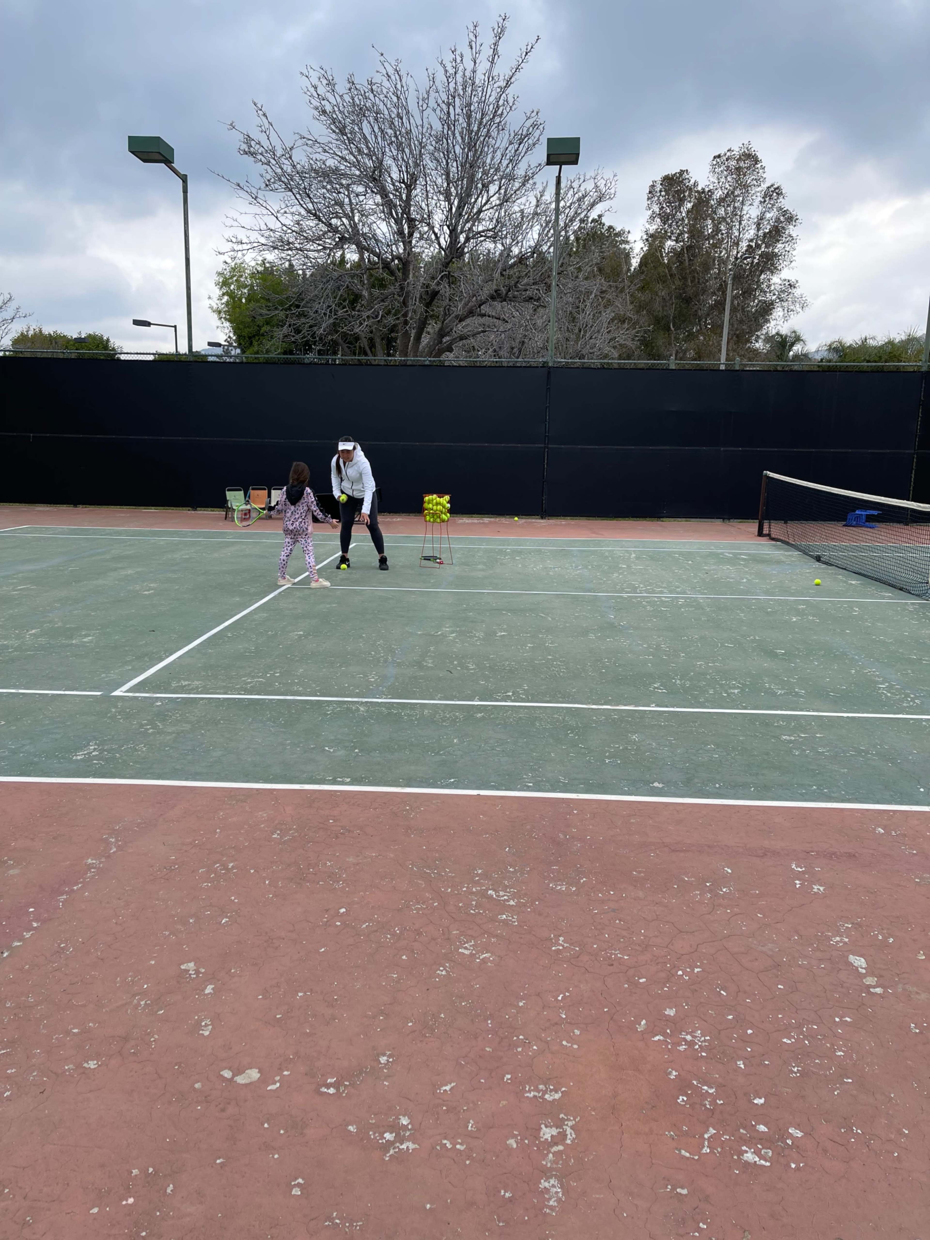 A coach demonstrates tennis strokes to a young girl on an outdoor court.