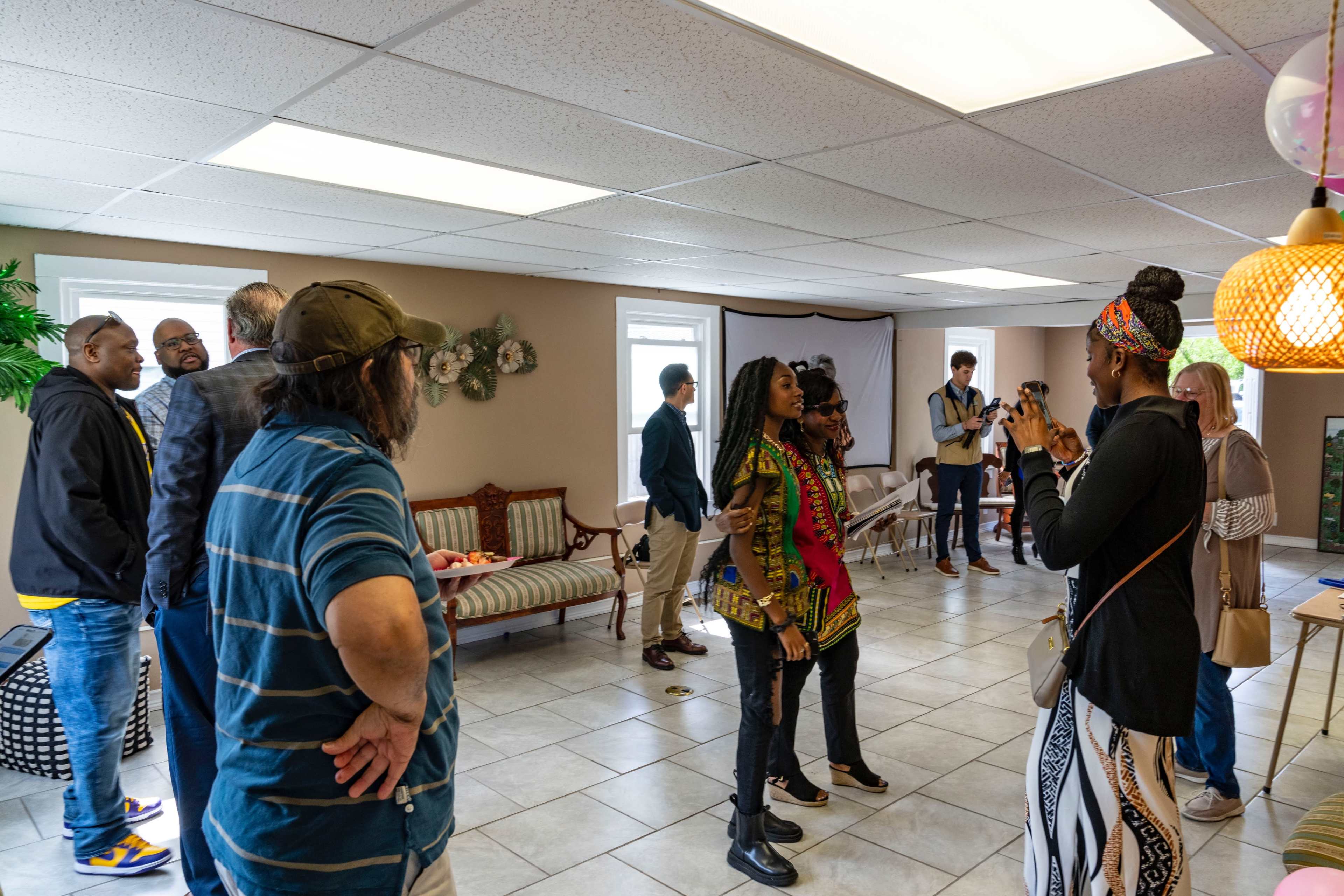 A group of people socializes in a spacious community room with tiled floors and bright lighting.