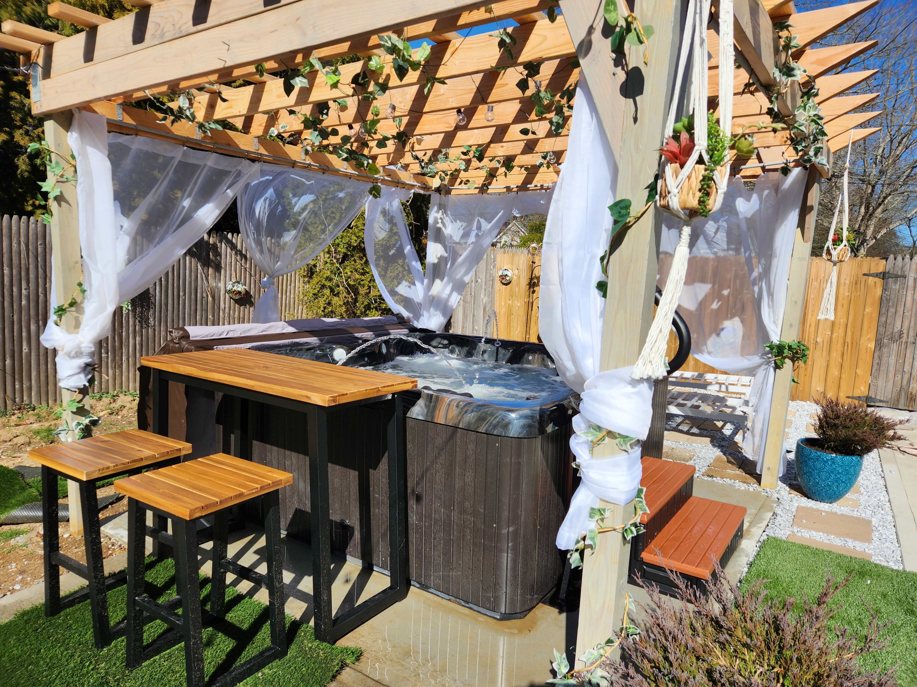 A spa area with a hot tub surrounded by wooden structures and tables, decorated with white drapes and greenery.