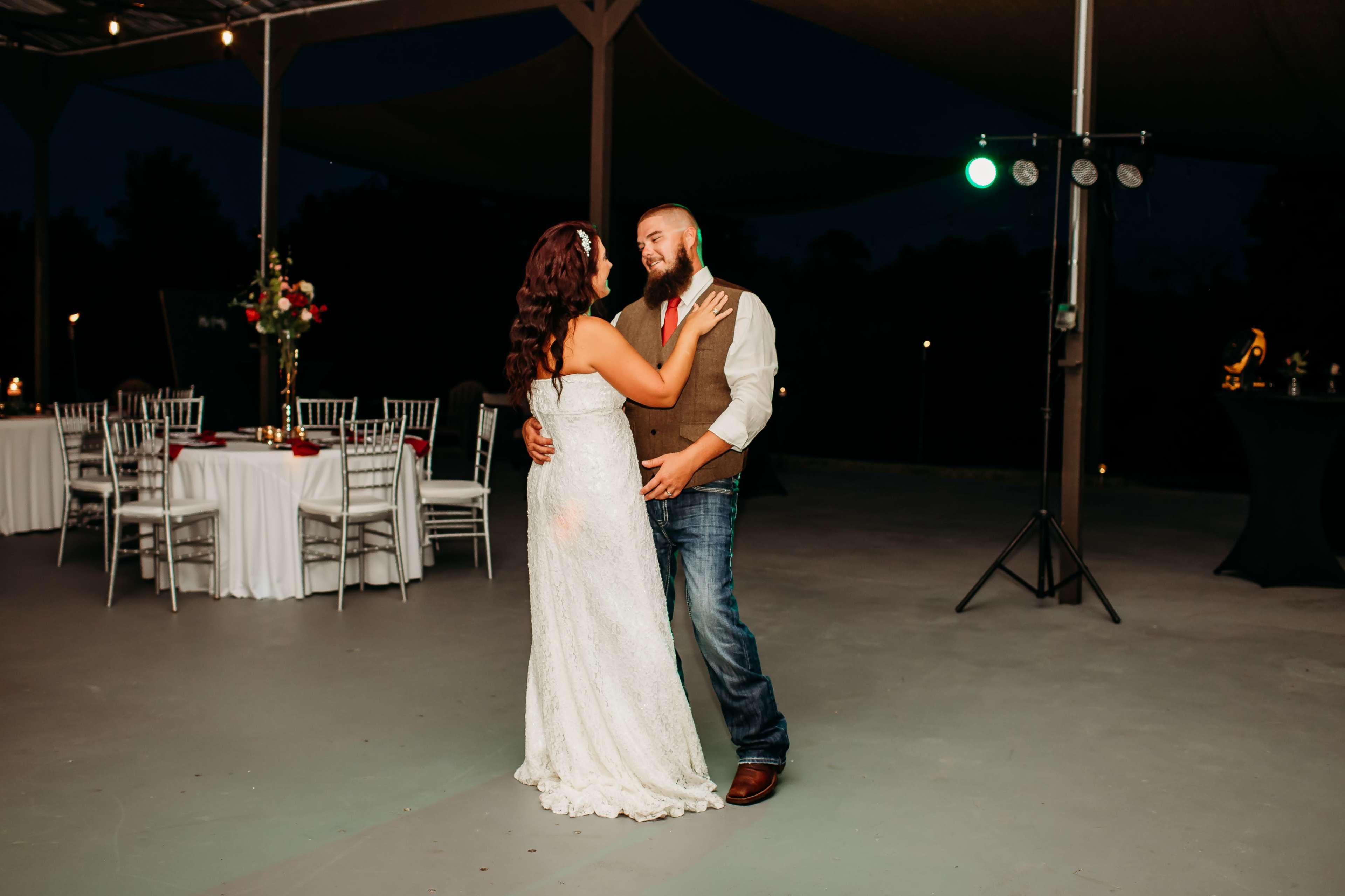 A couple dances closely on an outdoor patio, surrounded by elegantly set tables and soft lighting.