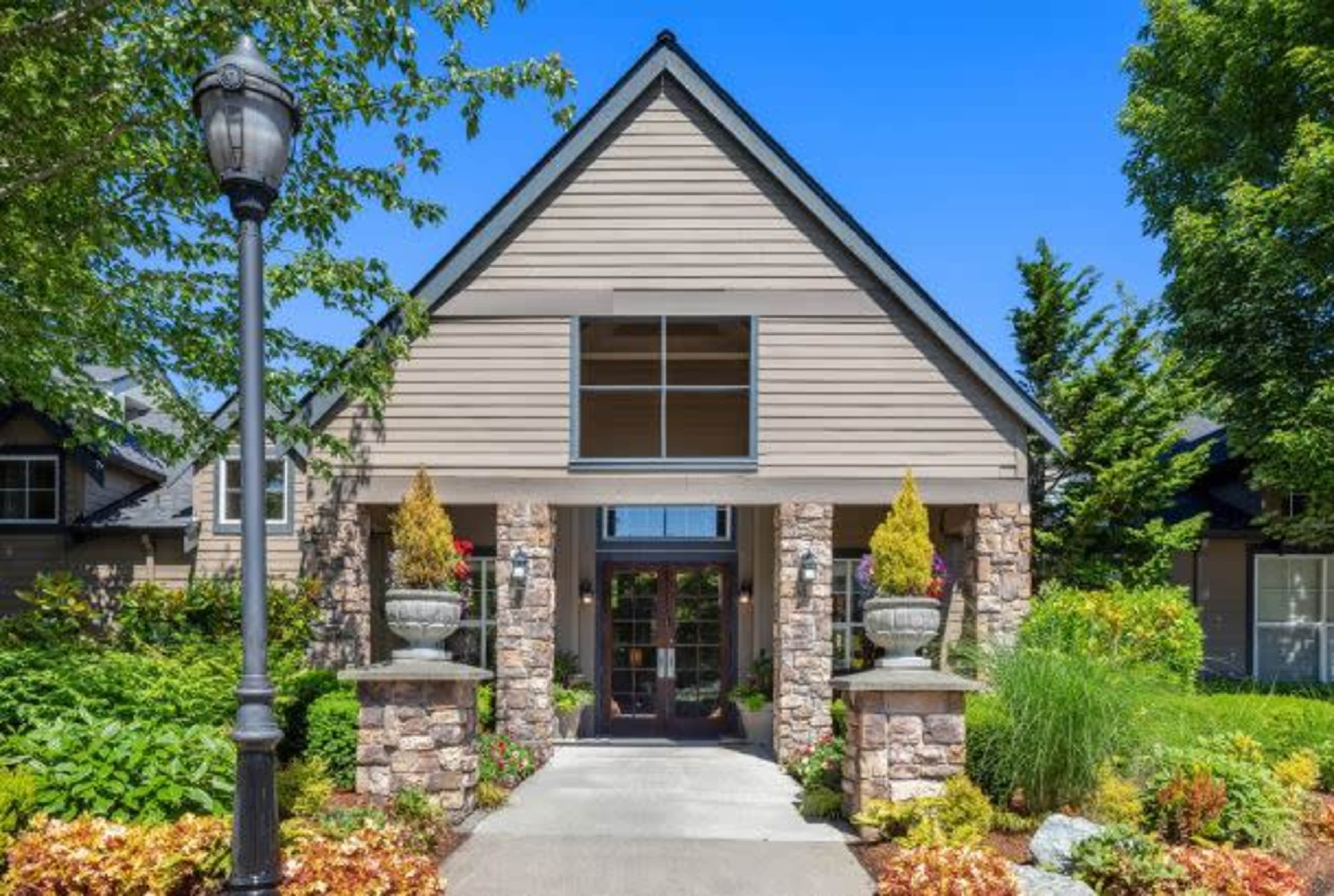 A modern house with a stone and wood exterior, featuring a wide front entrance flanked by decorative planters and surrounded by landscaped greenery.
