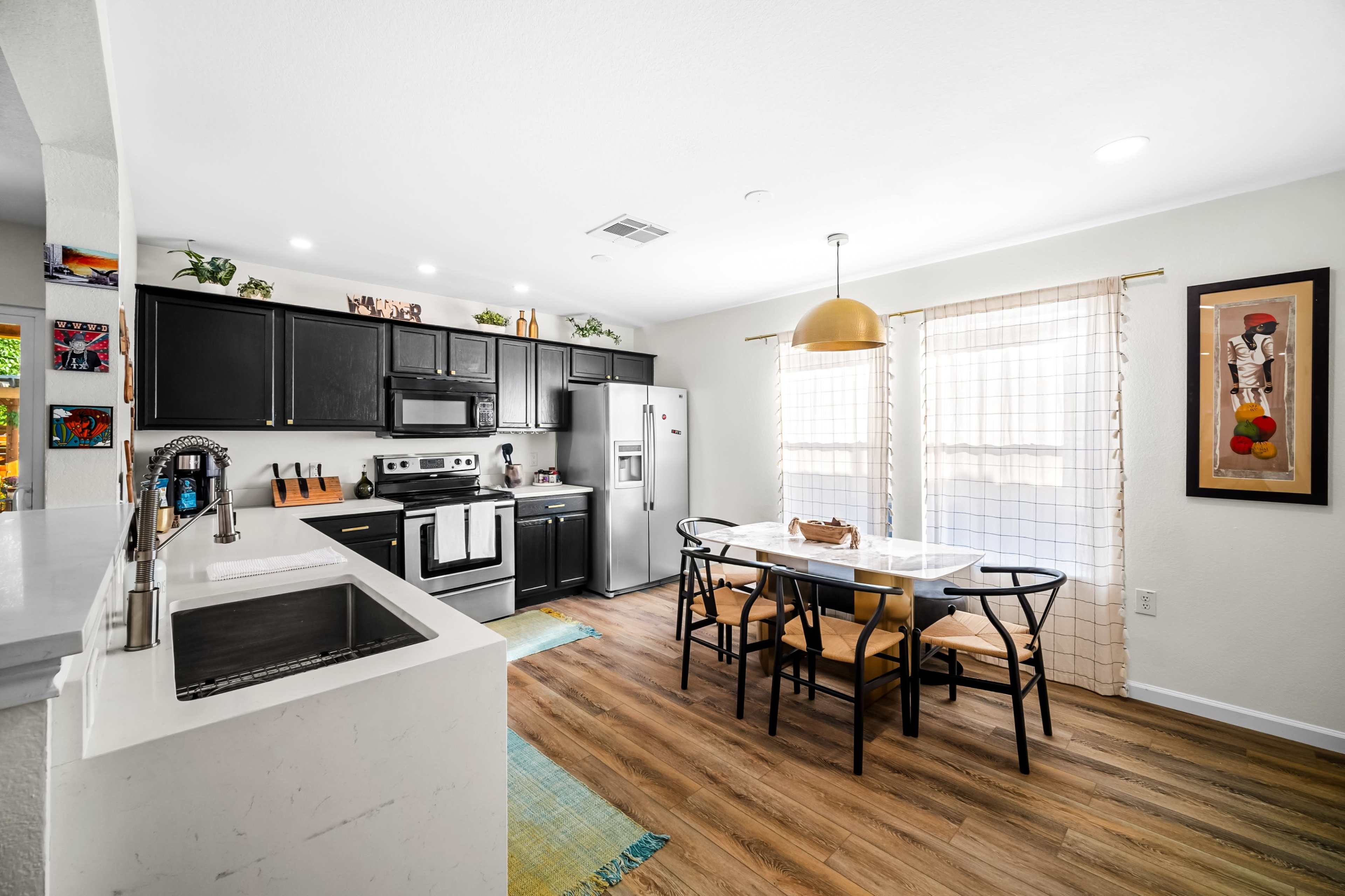 A modern kitchen features black cabinets, stainless steel appliances, and a dining area with a white table and black chairs.