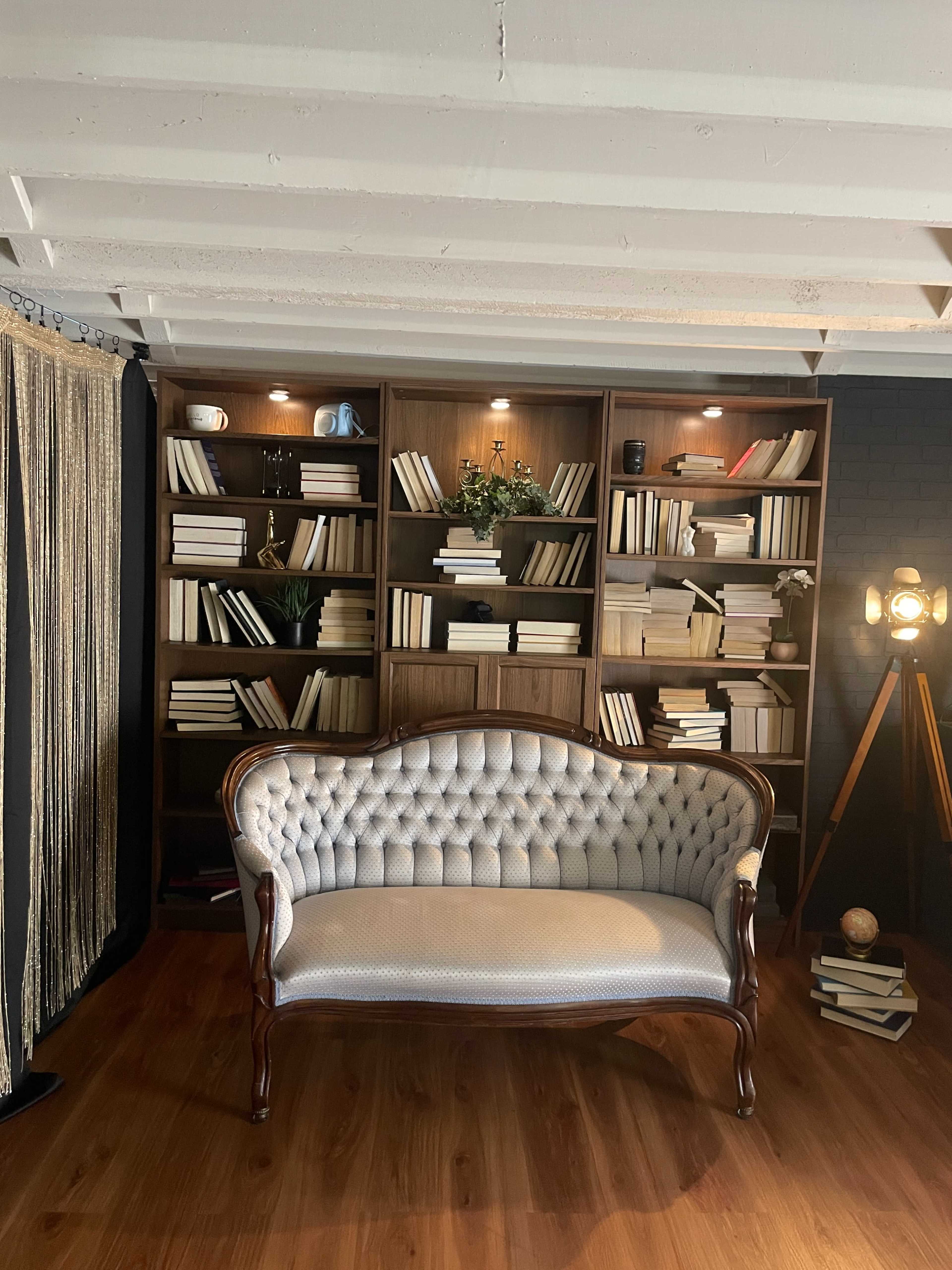 The image features a vintage tufted sofa positioned in front of a large bookshelf filled with neatly arranged books and decorative items.