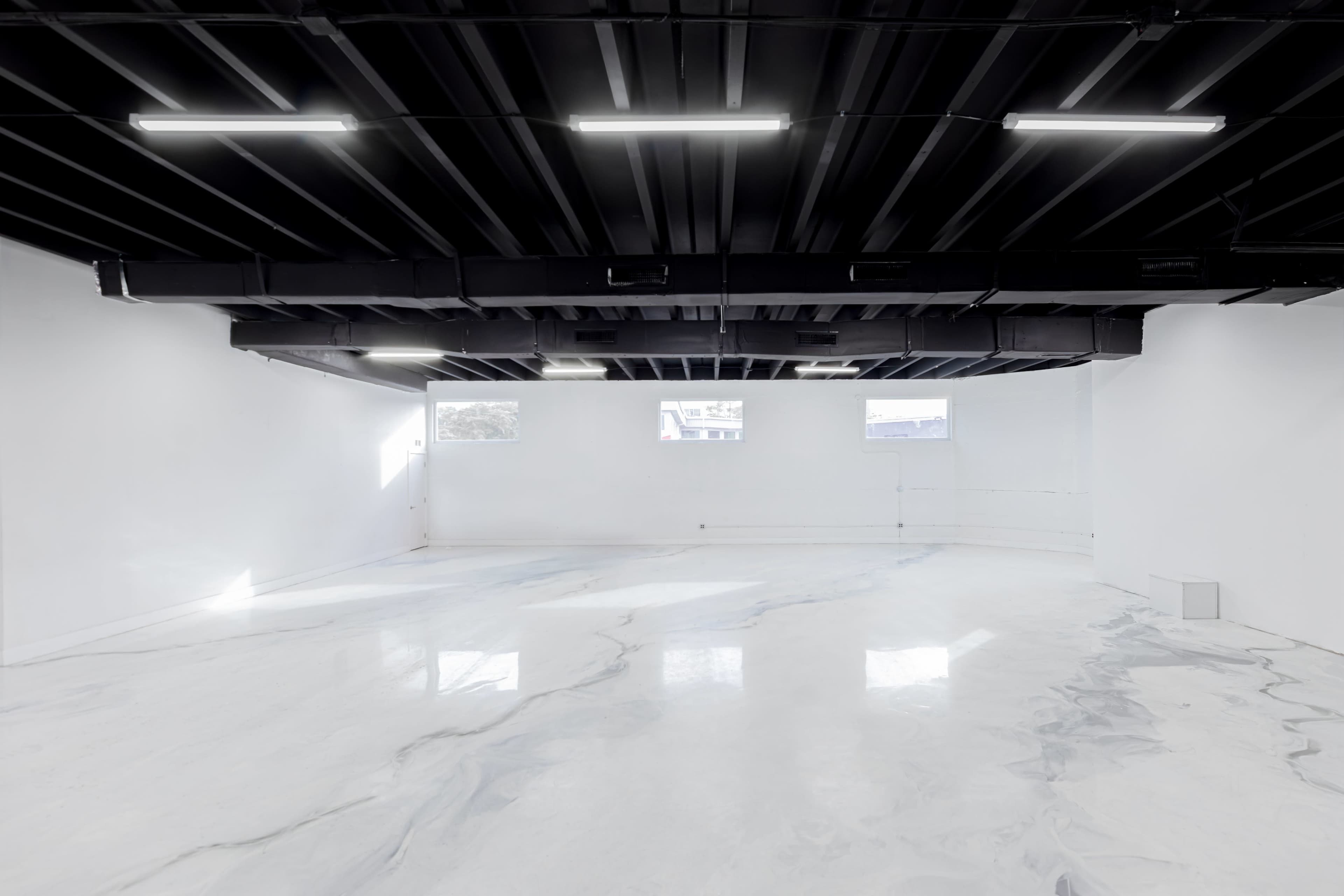 The image shows an empty, well-lit interior space with white walls, a black ceiling, and a marble-patterned floor.