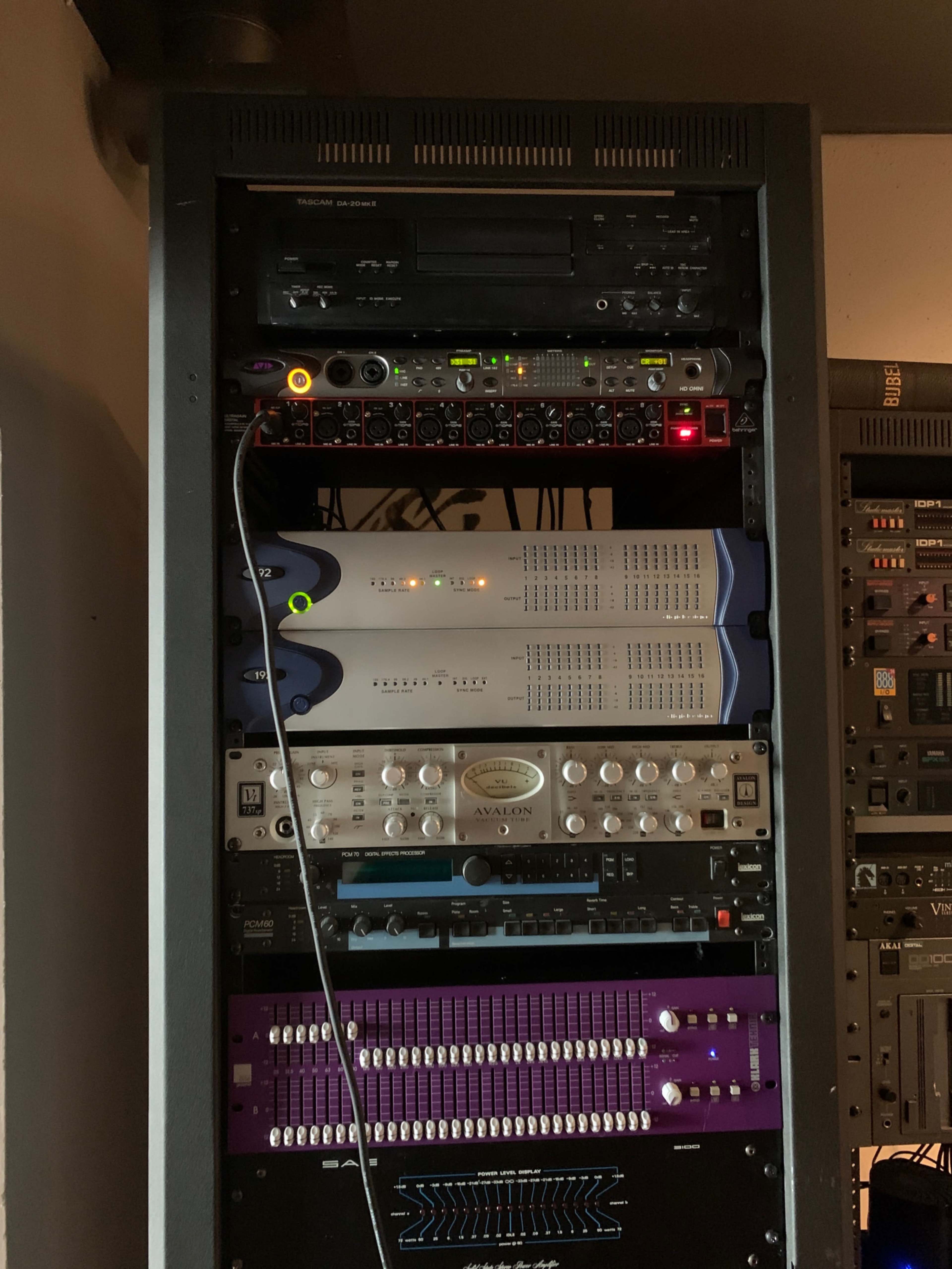 The image shows a rack-mounted audio equipment setup with various electronic devices, including mixers, processors, and interfaces stacked in a vertical arrangement.