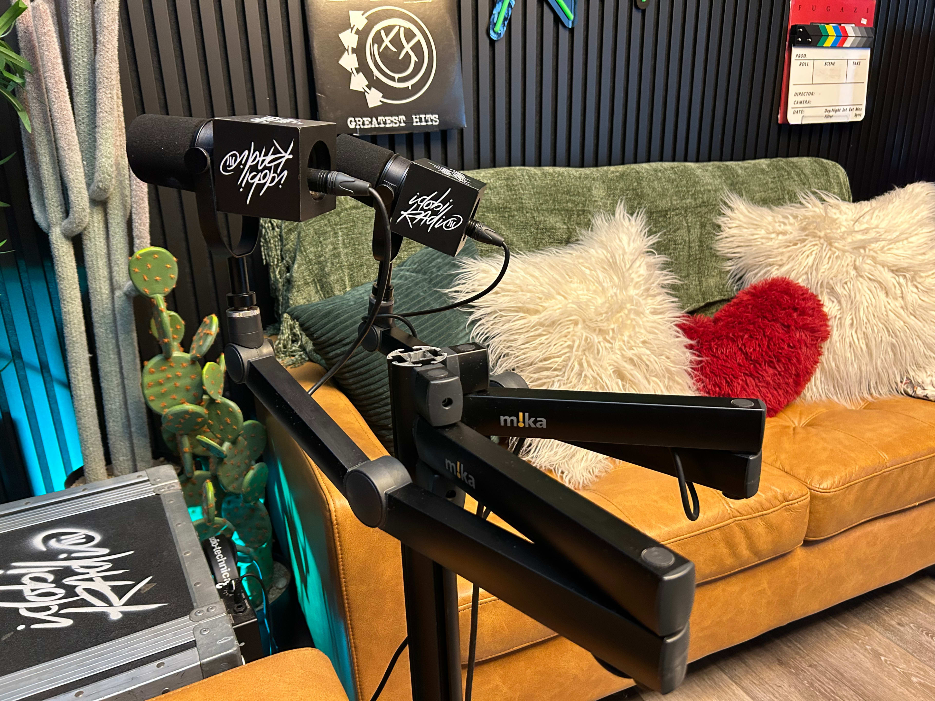 A microphone is mounted on a stand in front of a couch adorned with pillows and decorative elements in a colorful, modern studio setting.